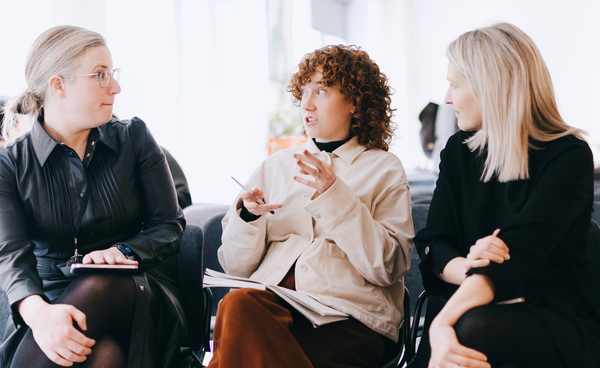 Three women engage in a thoughtful discussion about sustainability during a meeting at the University of Glasgow.