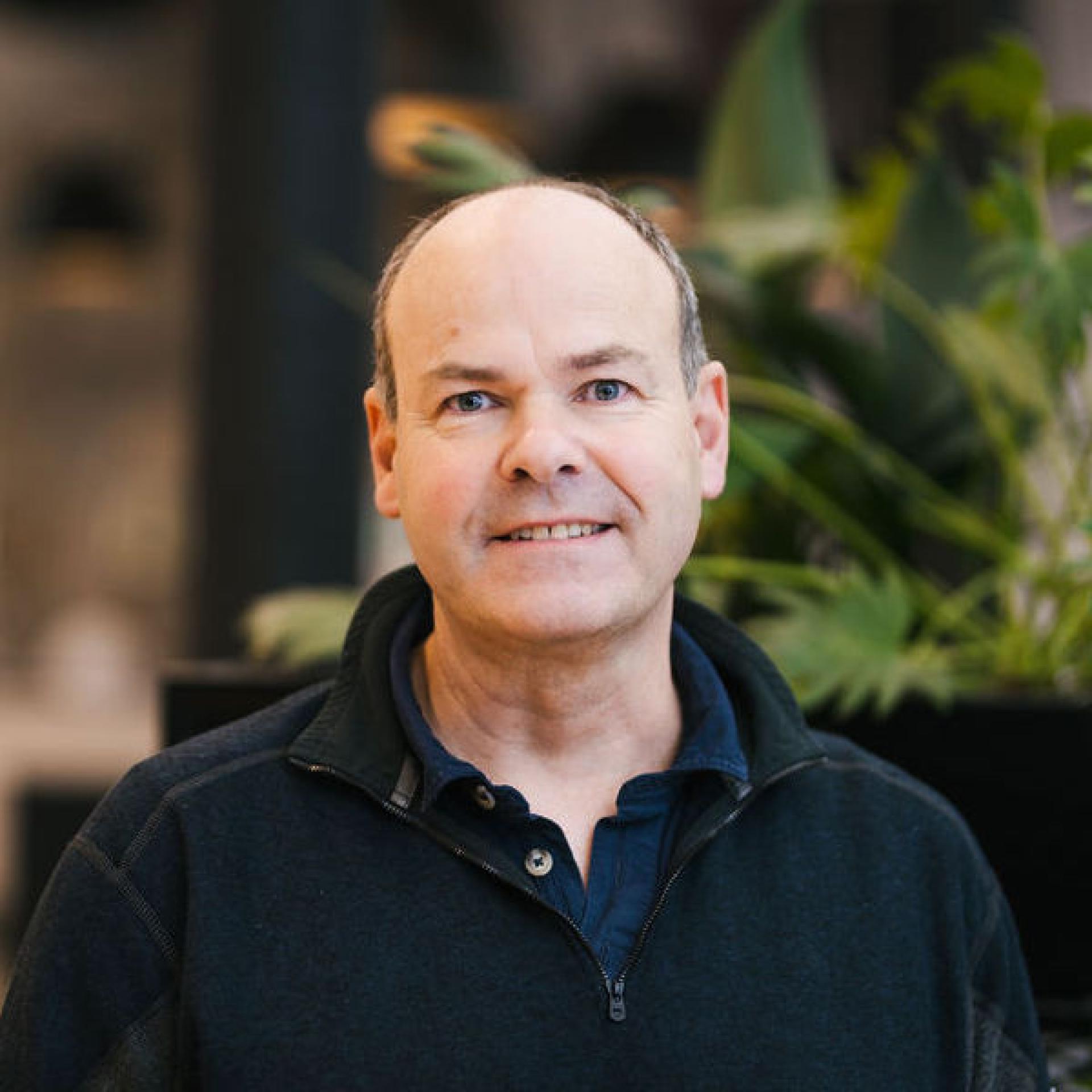 Professional man smiling in an indoor setting with greenery, discussing Glasgow's property outlook and future trends.