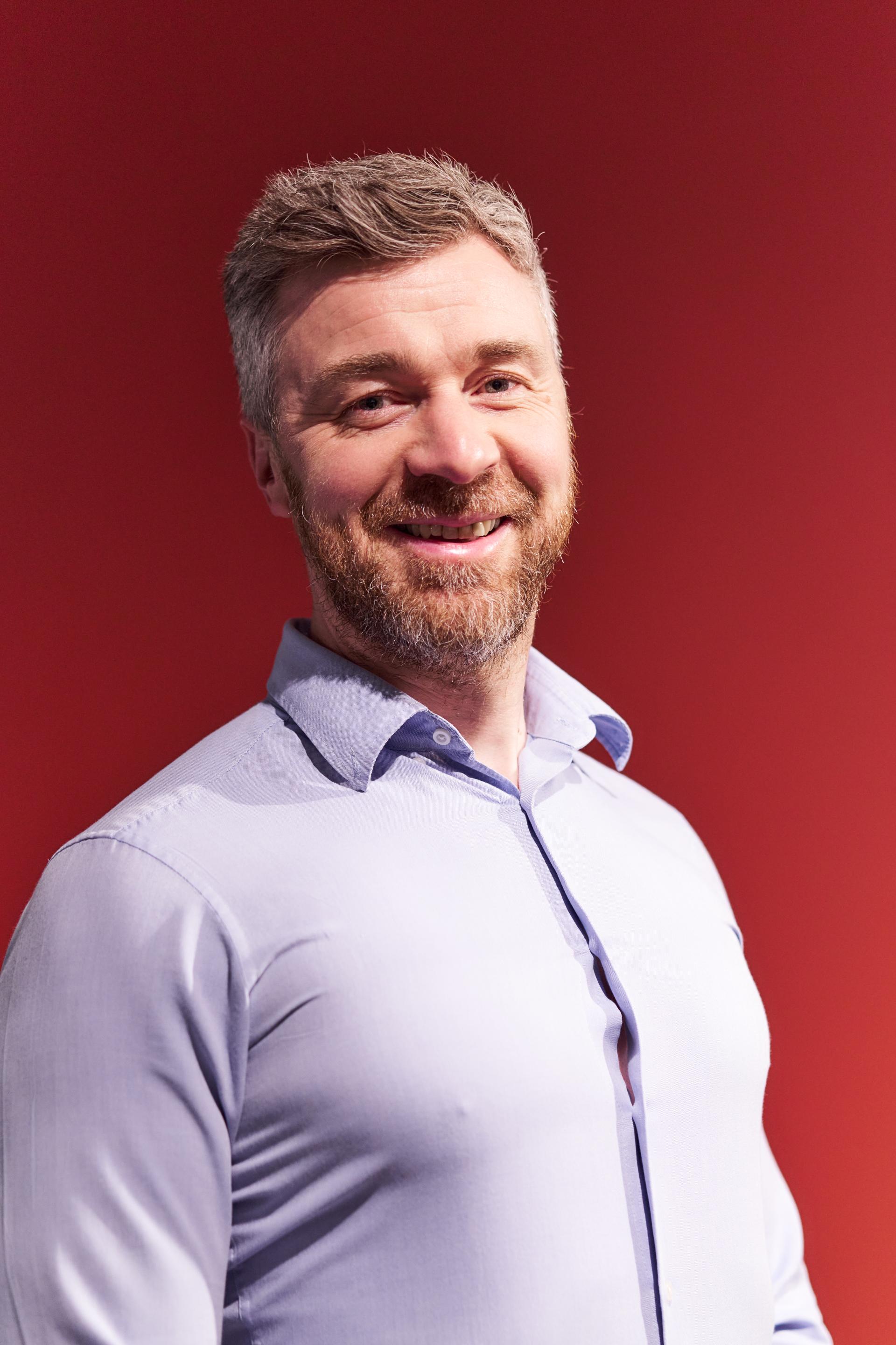 Smiling man in a light blue shirt against a red background, highlighting Glasgow's residential discussion.