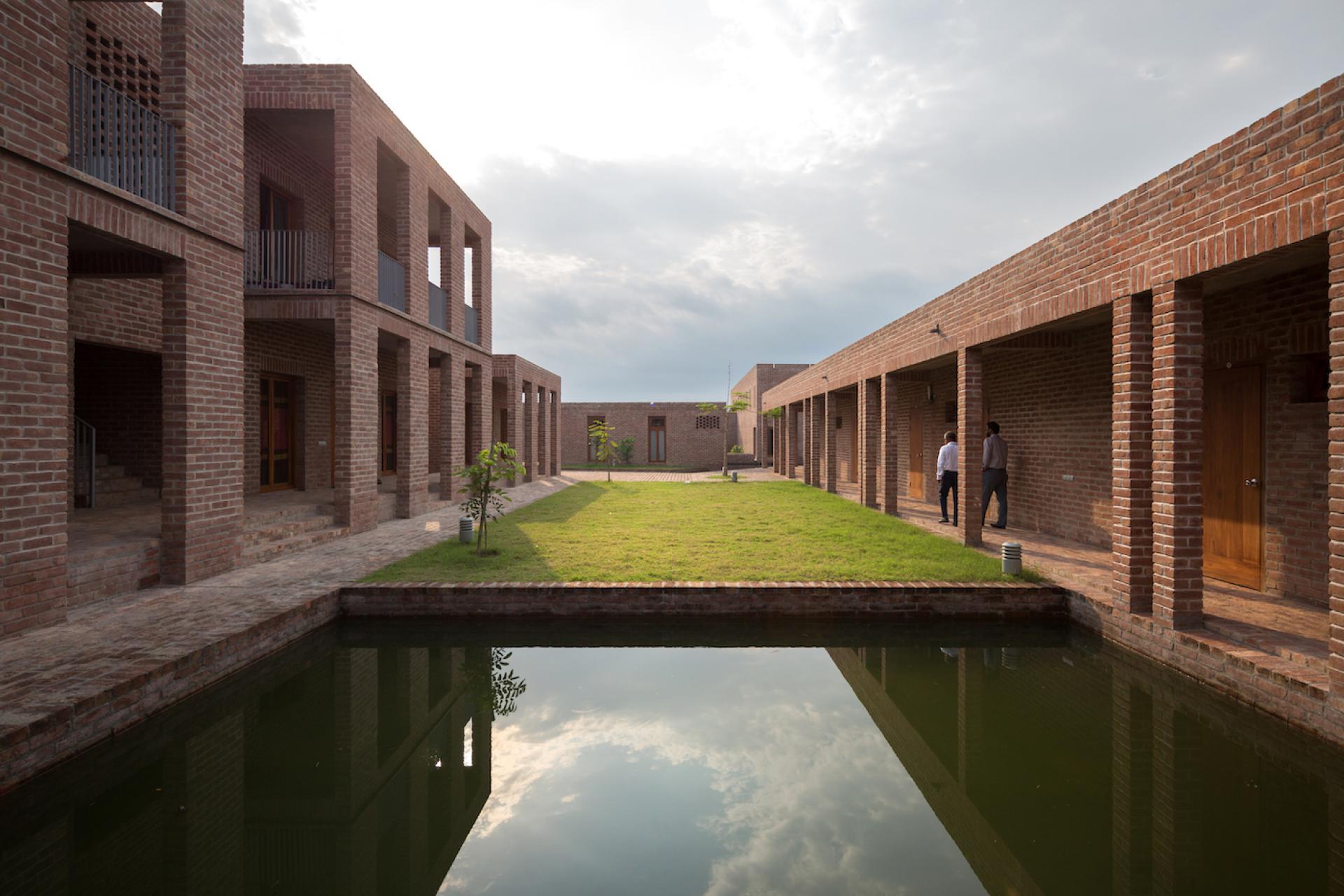 Modern community hospital in Bangladesh, showcasing brick architecture, green landscaping, and serene water features.
