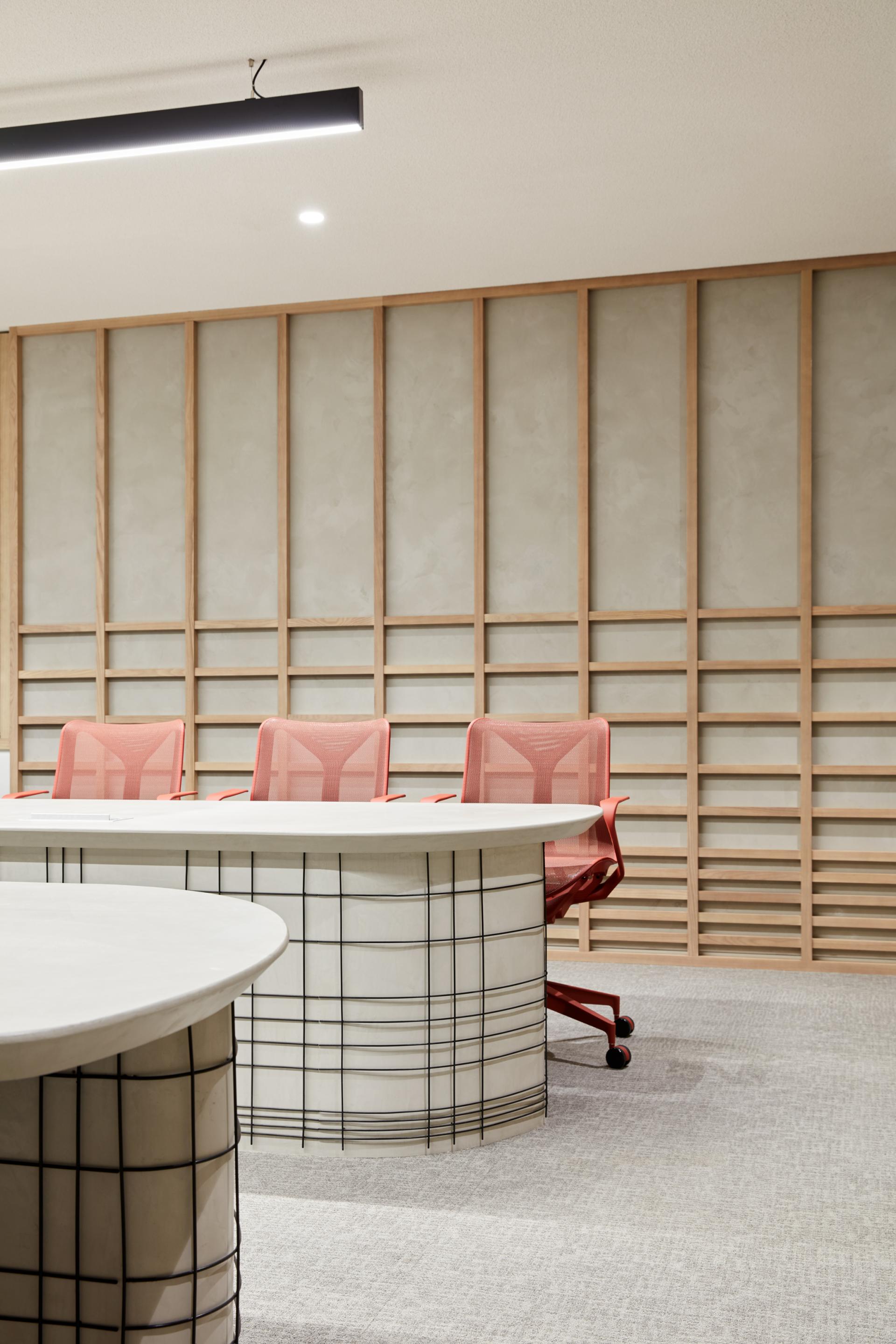 Modern conference room featuring a sleek, round table with grid design and contemporary red chairs, showcasing a blend of Japanese and Emirati aesthetics.