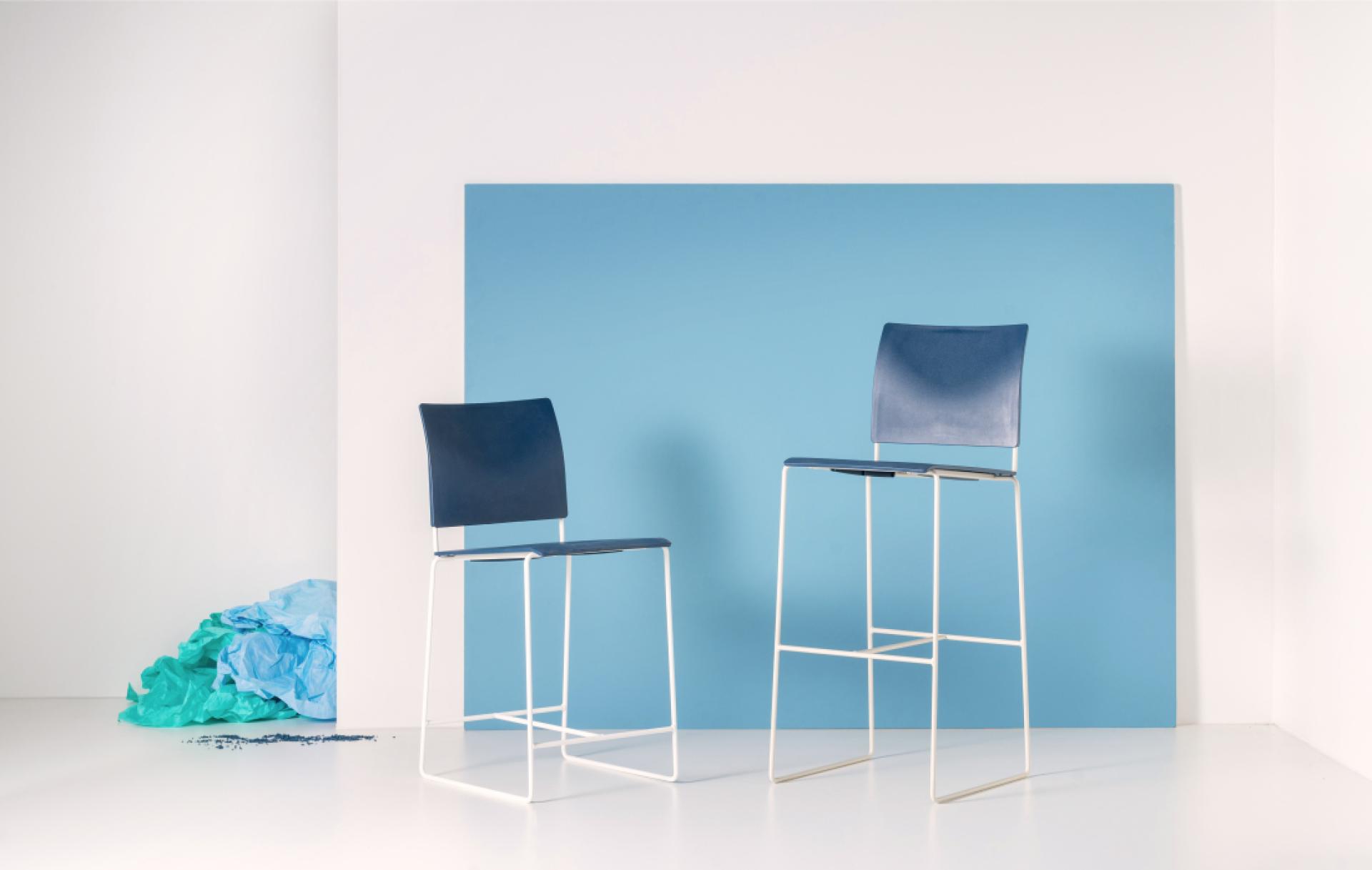 Modern bar stools with blue seats against a light blue backdrop, showcasing sustainable design innovation for 2022.
