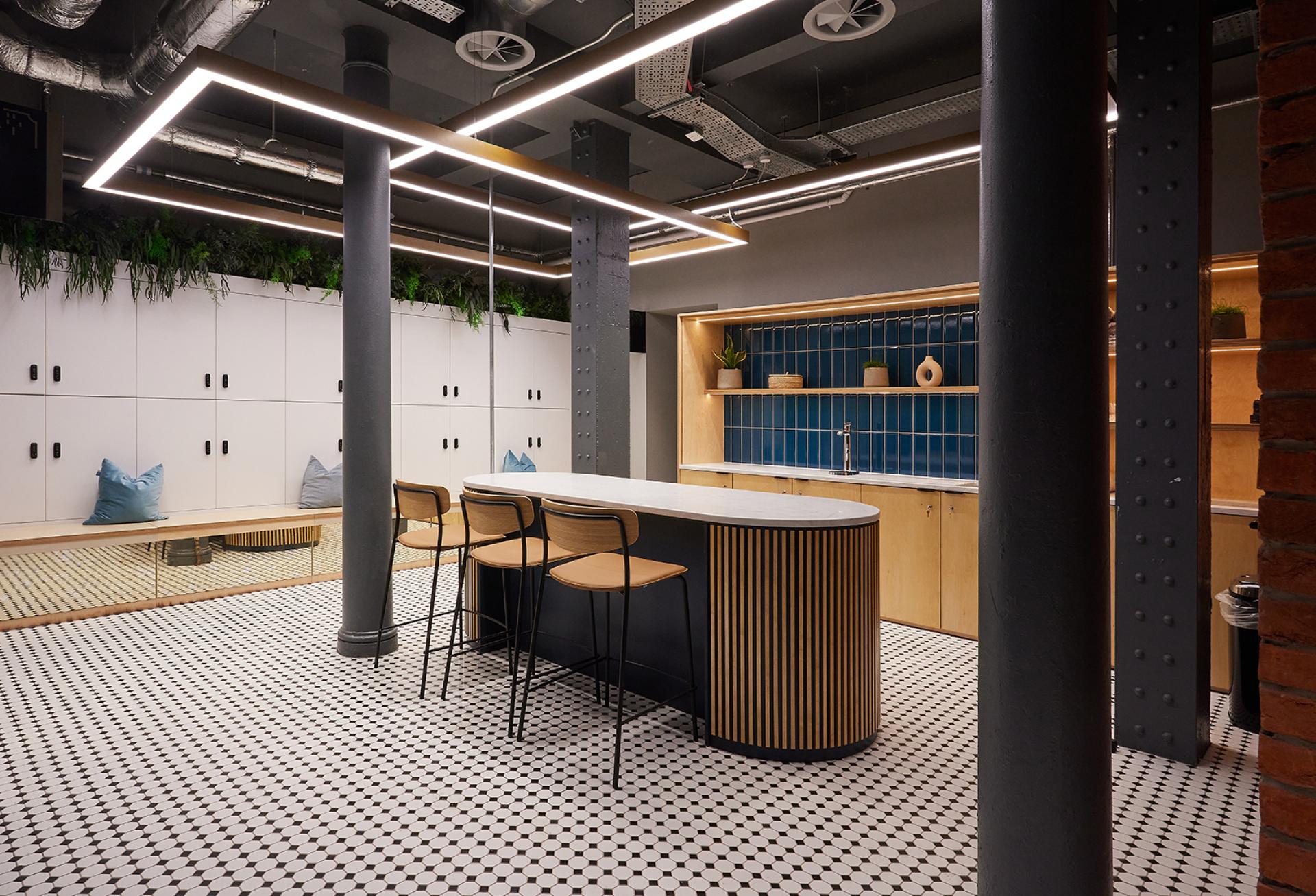Modern office kitchen at Michael Laird Architects featuring stylish bar seating, blue tiles, and natural plants.