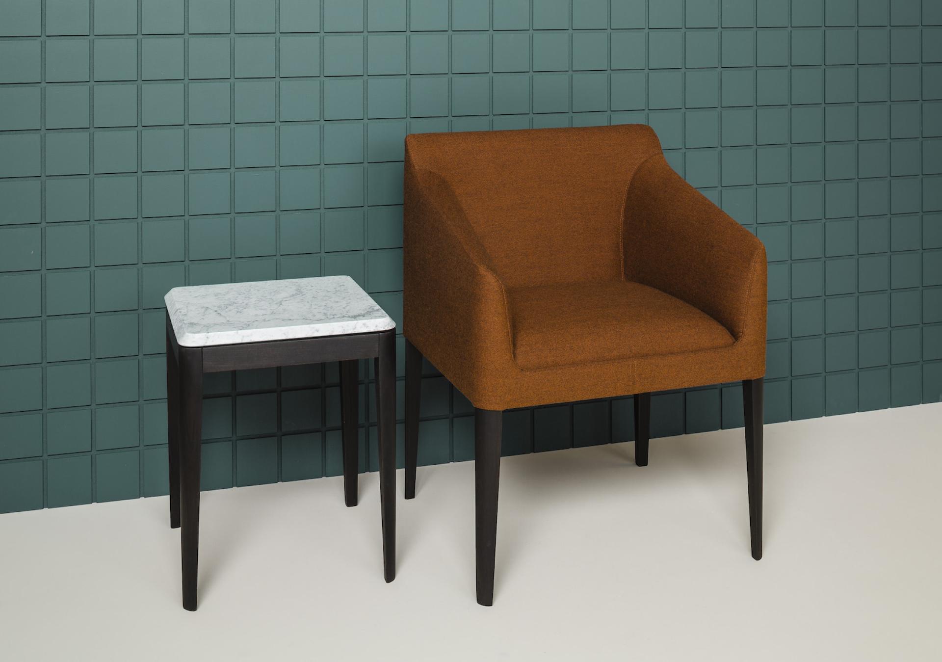 Stylish brown chair next to a small marble-topped table against a green textured wall, embodying modern interior design.