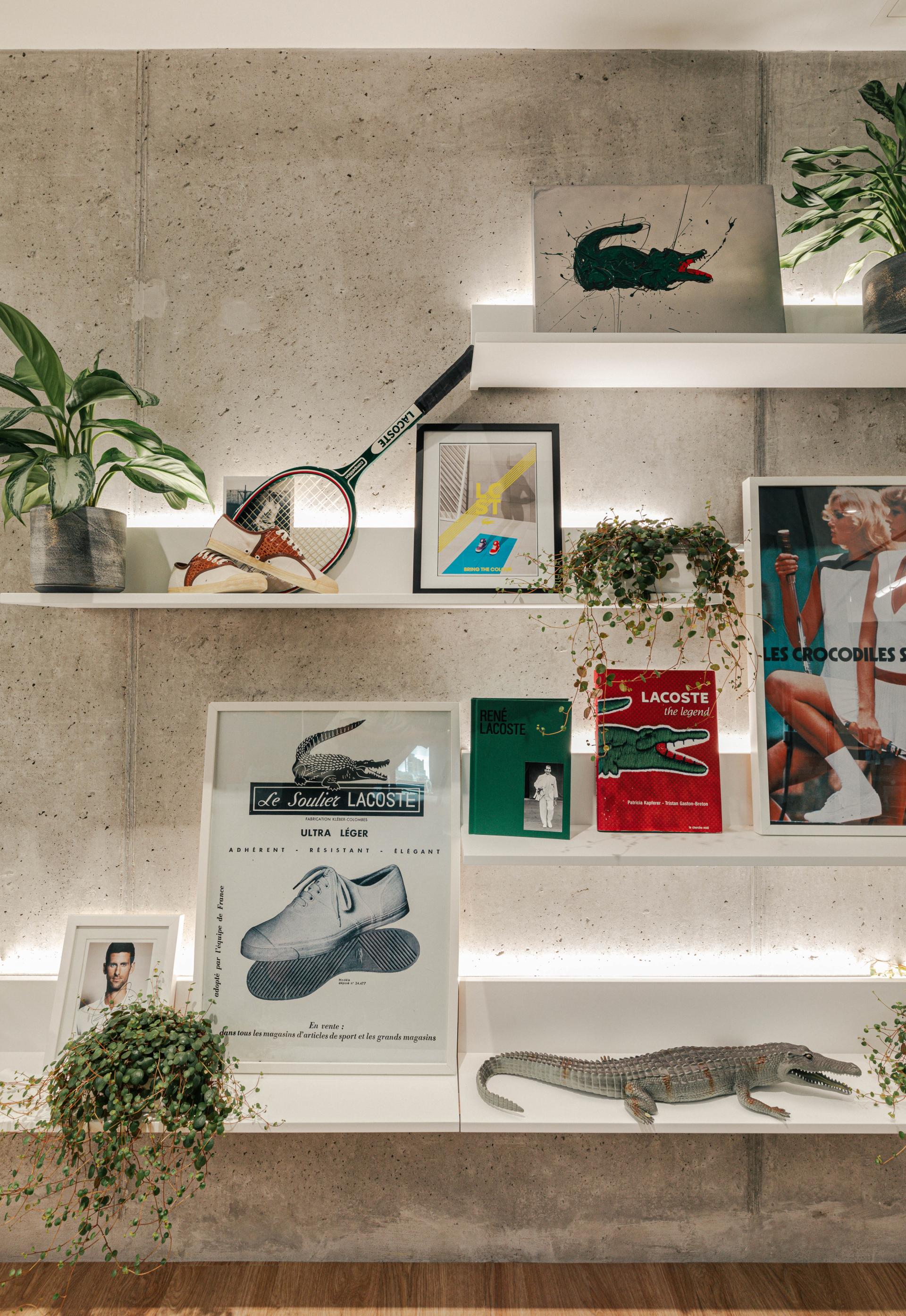 Lacoste-themed workspace decor featuring tennis rackets, shoes, and iconic crocodile imagery on shelves with a modern aesthetic.