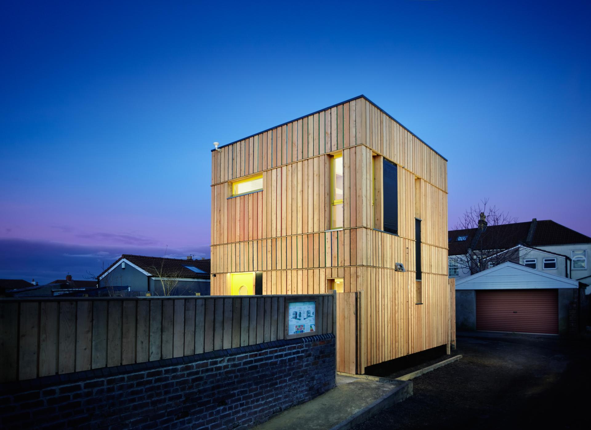 Modern wooden house illuminated at dusk, showcasing innovative architectural design nominated for Wood Awards 2021.
