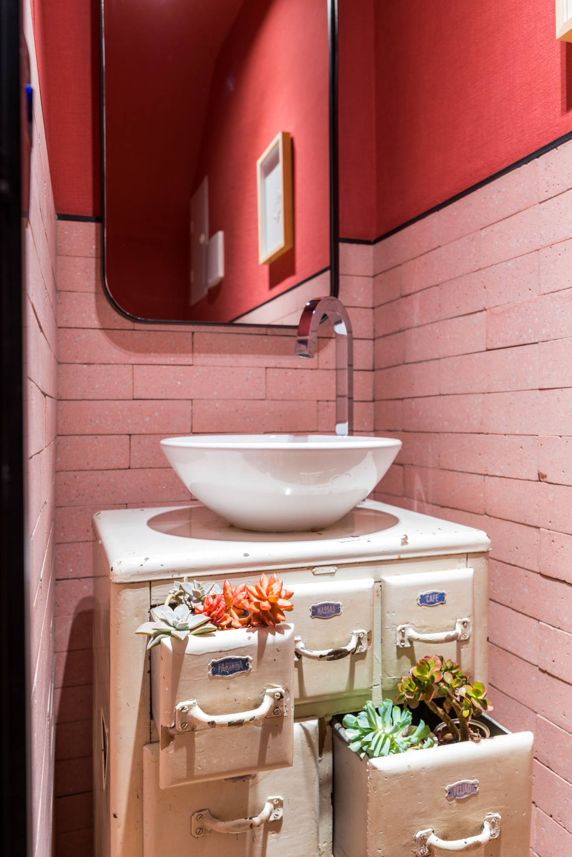 Stylish bathroom with a unique sink atop vintage drawers, adorned with succulents and a vibrant red backdrop.