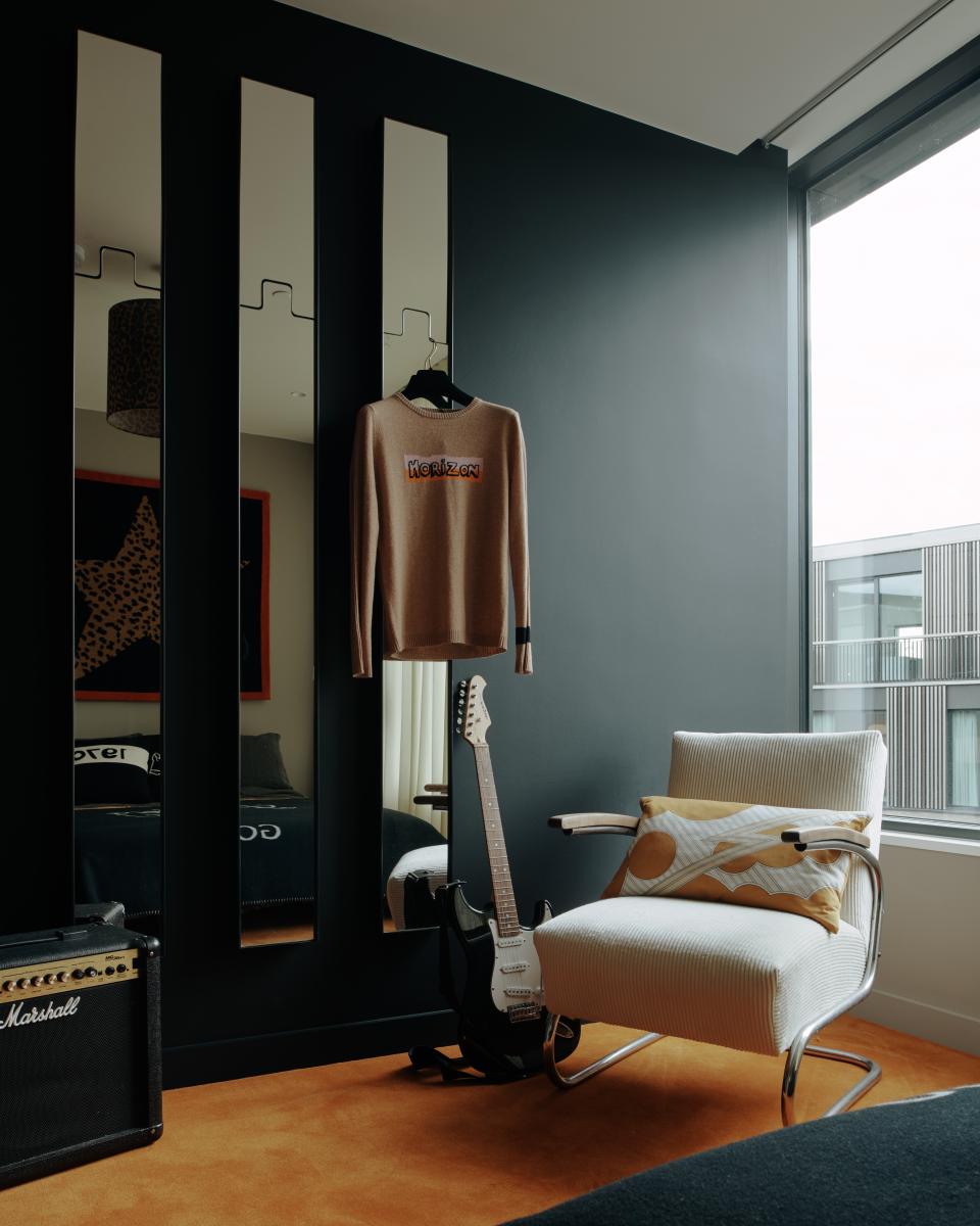 Elegant interior featuring Bella Freud's sweater, a guitar, and a modern armchair in a stylish bedroom setting.