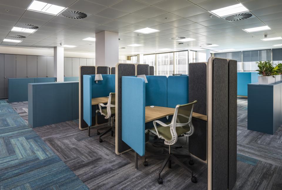 Modern office workspace featuring ergonomic desks, blue acoustic panels, and natural light in WELL certified design.