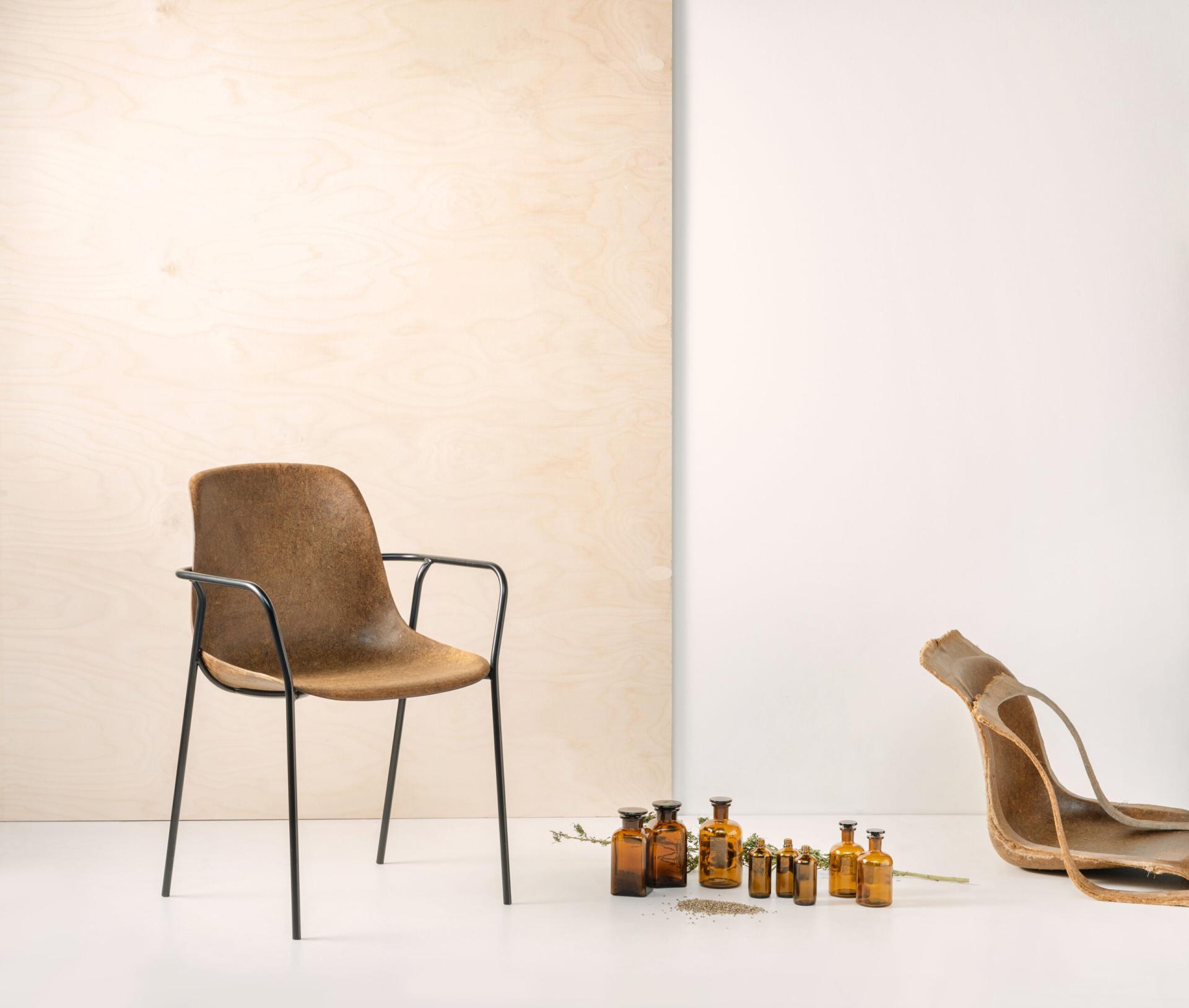 Sustainable Vepa chair made from natural materials, surrounded by glass bottles and a leather piece on a light backdrop.