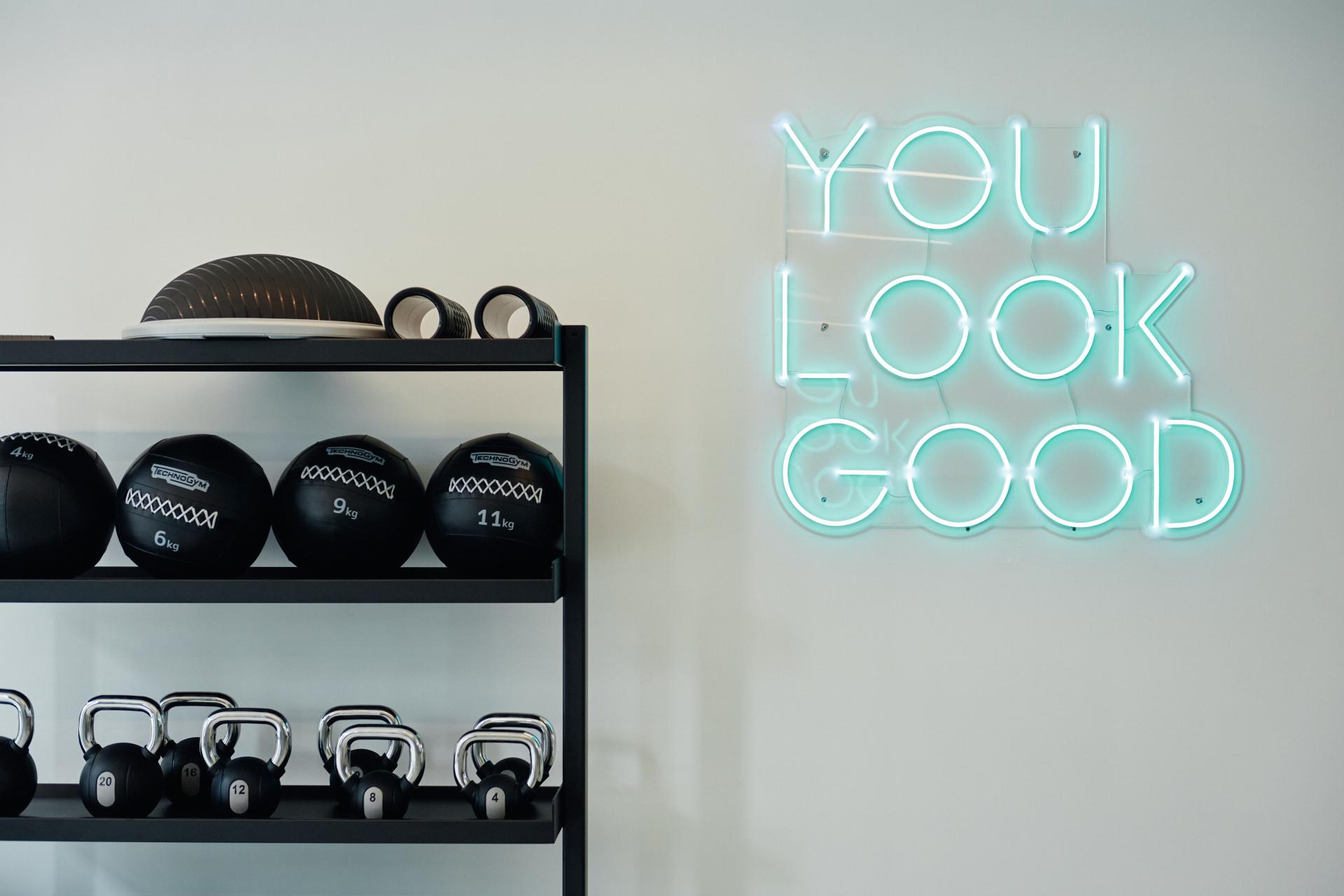Modern fitness area featuring black weights, kettlebells, and a motivational neon sign at The Headline, Leeds.