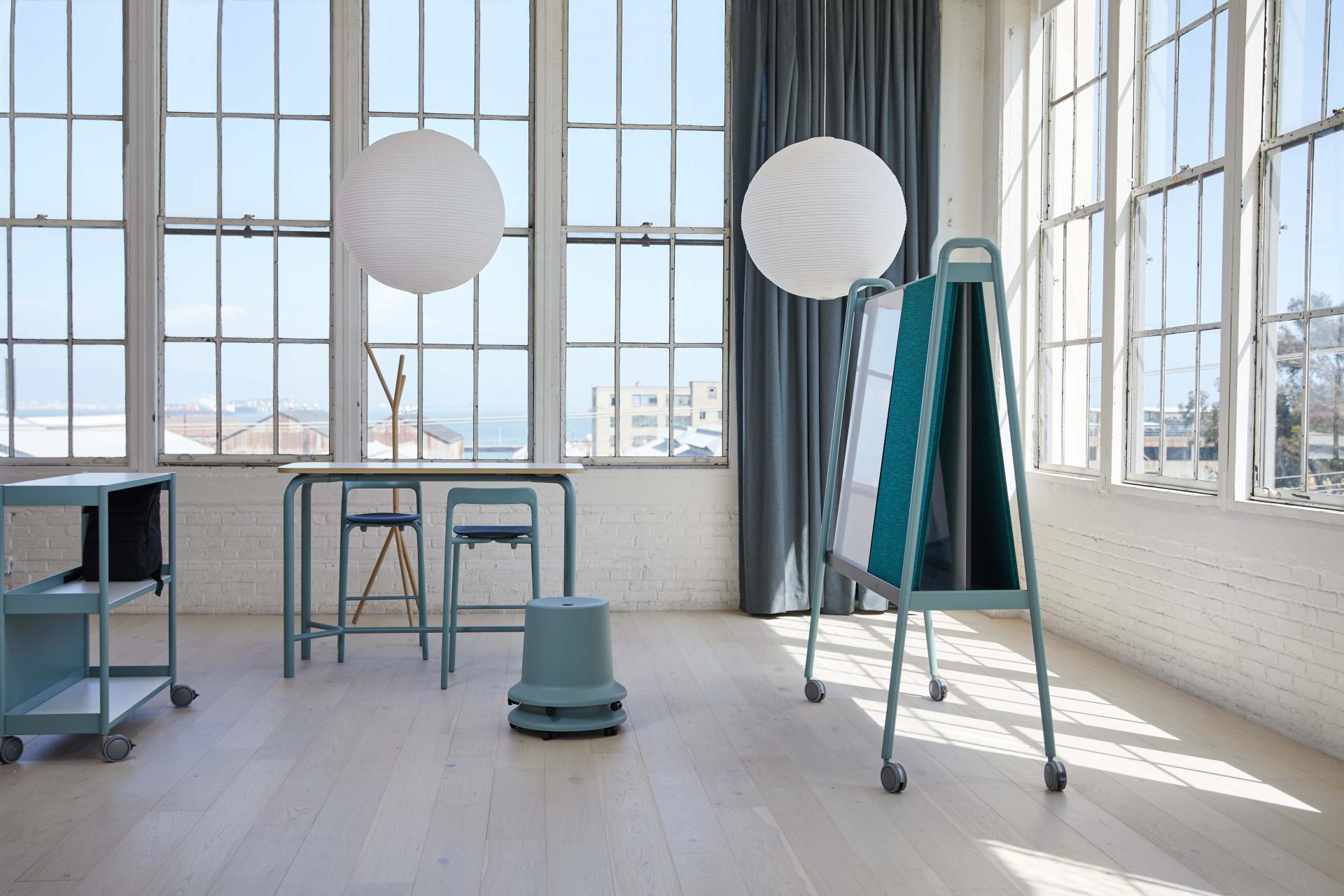 Versatile workplace furniture from Pearson Lloyd's Routes collection, featuring a desk, seating, and mobile partition in a bright space.