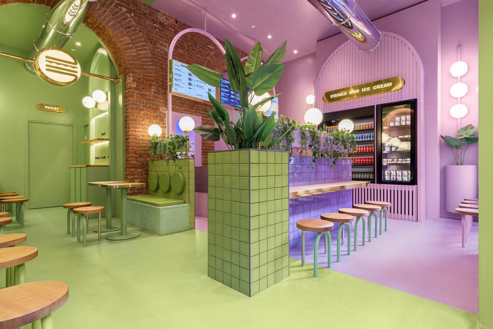 Vibrant candy-colored interior of Bun restaurant in Milan featuring green and purple tones, modern seating, and lush plants.