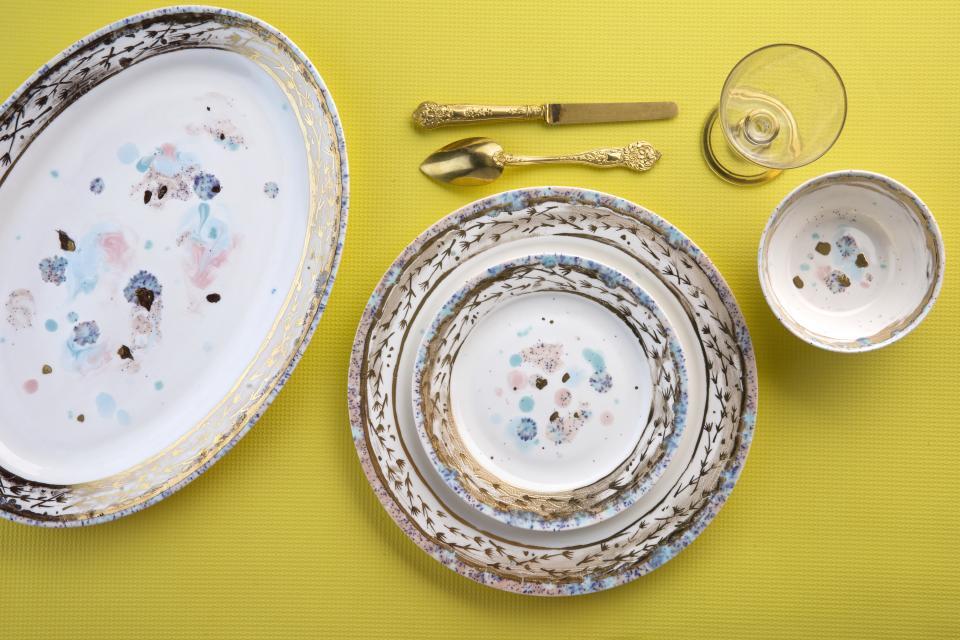 Hand-decorated ceramic and porcelain tableware by Coralla Maiuri displayed on a vibrant yellow background.