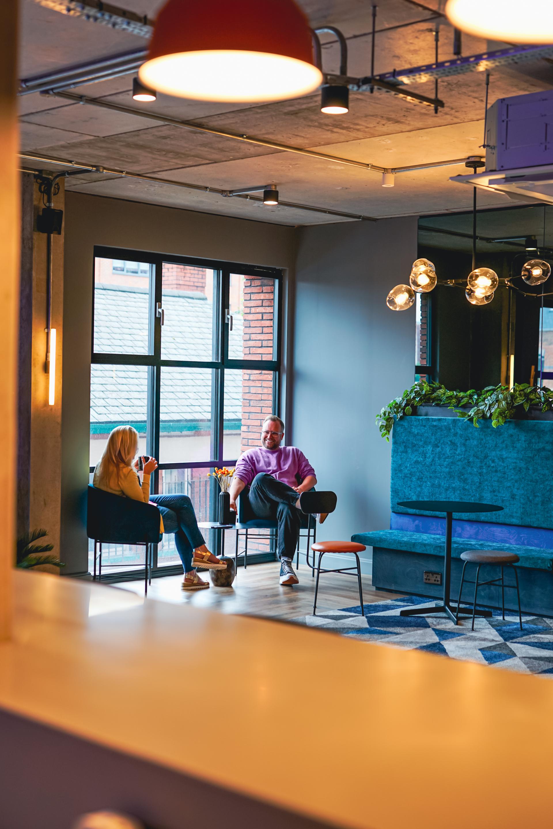 Two professionals enjoying coffee in a stylish, modern workspace with large windows and vibrant decor.