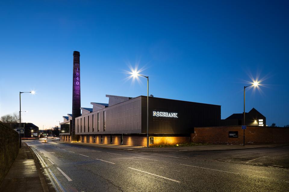 Renovated Rosebank Distillery at dusk, showcasing modern architecture alongside the original historic chimney, blending heritage and innovation.