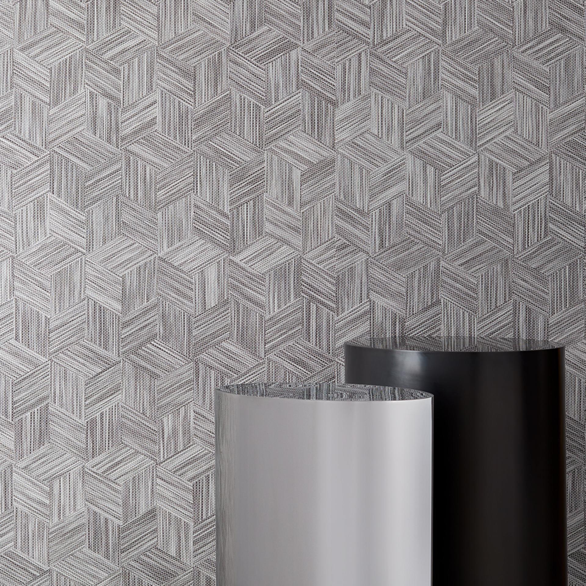 Textured wallcovering featuring a geometric pattern in neutral tones, alongside two cylindrical rolls in silver and black.