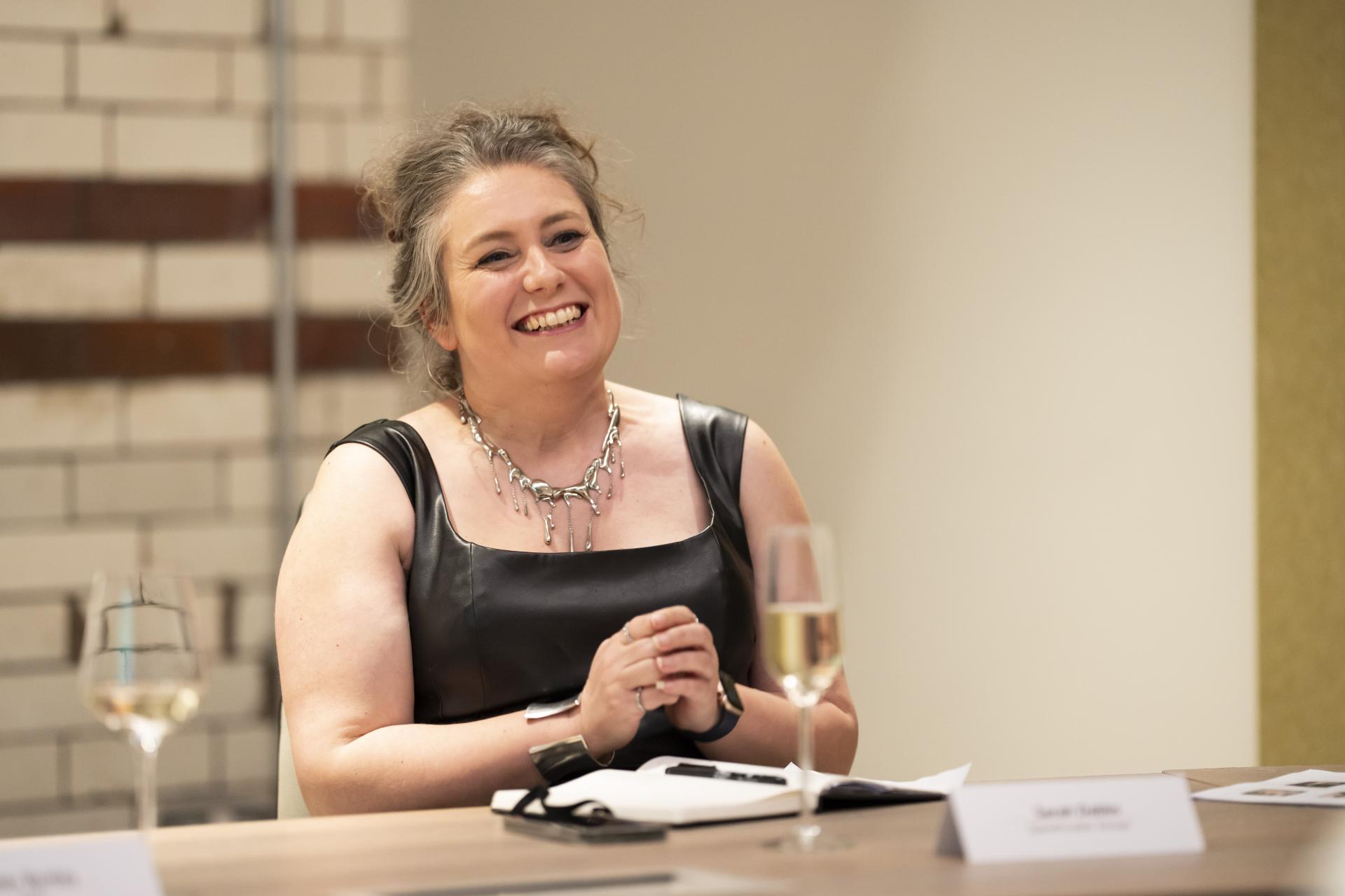 Senior design expert engaged in discussion about technology and sustainability in design, smiling and seated at a table.