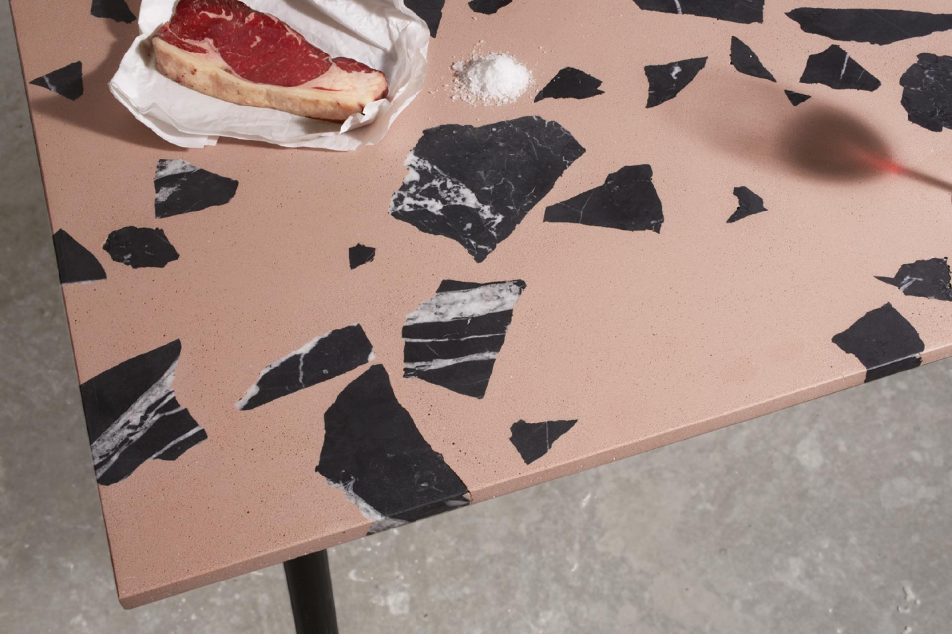 Alt text: A stylish tabletop featuring pink surface and black marble accents, with a steak and salt nearby, showcasing innovative design.