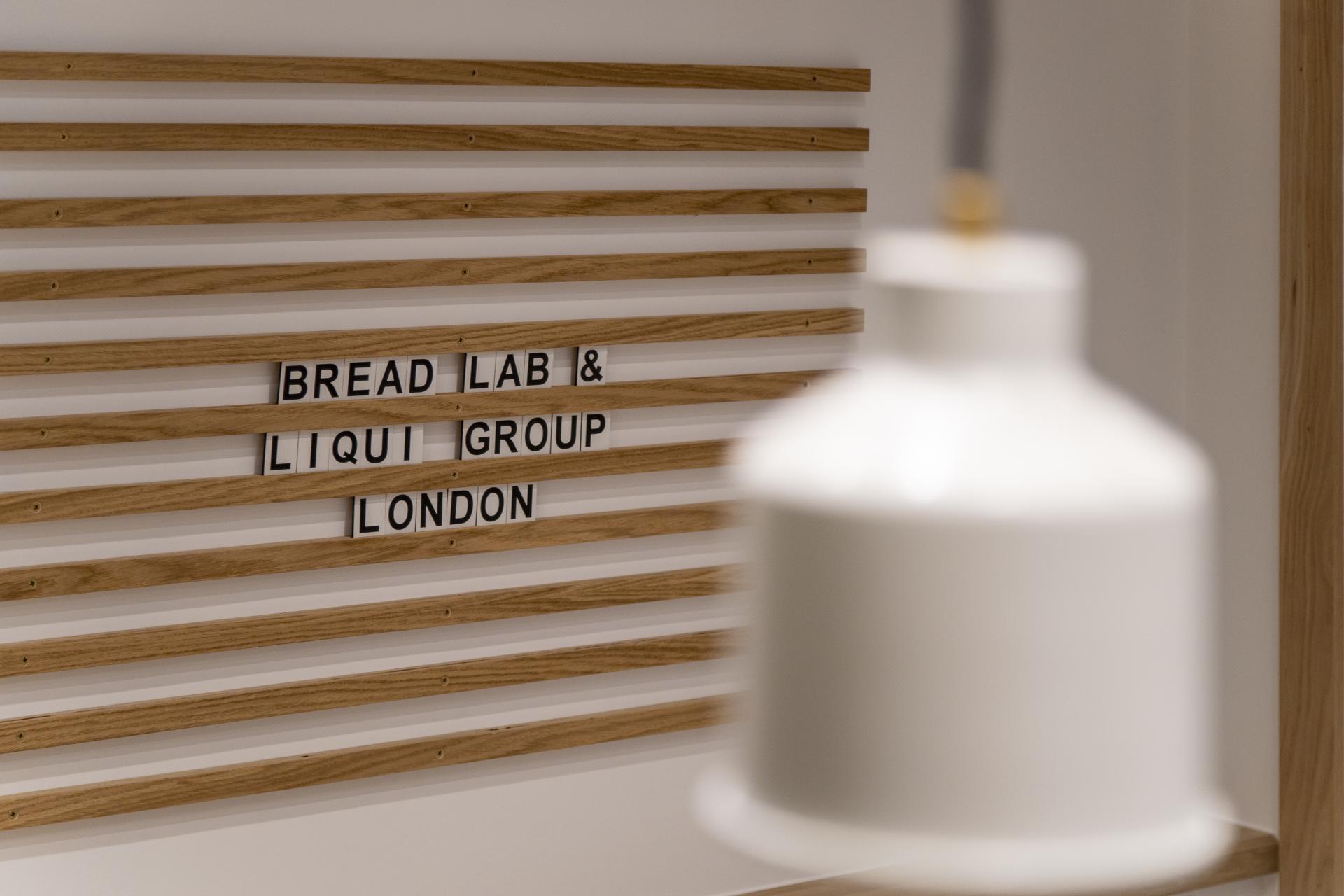 Minimalist wooden wall design featuring the "Bread Lab & Liqui Group London" sign, highlighting the bakery's contemporary interior.