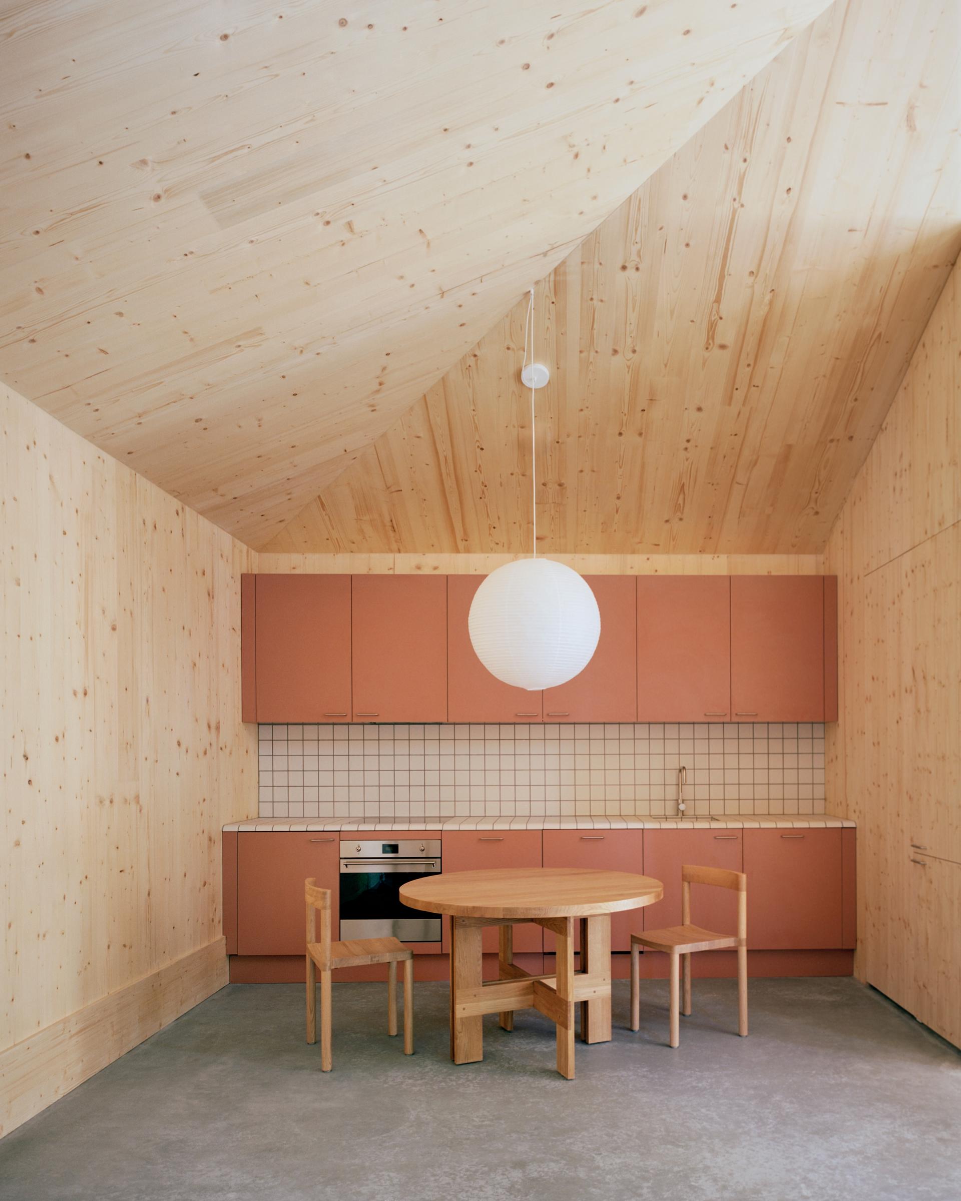 Minimalist kitchen featuring sustainable wood materials, soft pink cabinets, and a round wooden dining table.