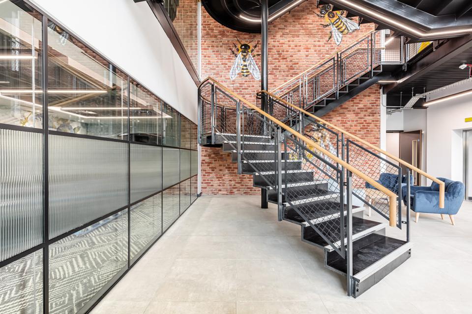 Modern staircase in the Bee House office, featuring brick walls and contemporary design elements for flexible workspace aesthetics.