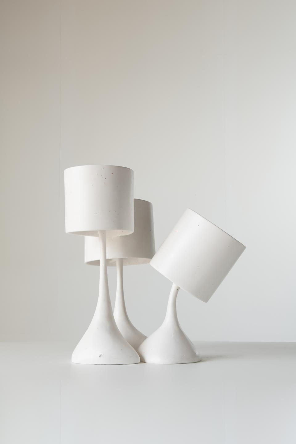 Contemporary white ceramic lamps with unique shapes displayed against a minimalistic backdrop at Reynold Rodriguez's solo show.
