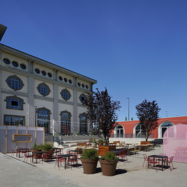 Redeveloped former thermal power plant in Bergamo, featuring outdoor seating areas and modern architecture in a vibrant community space.