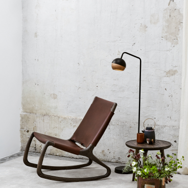Elegant rocking chair by Mater, designed by Shawn Place, with a sleek modern lamp and decorative plant table.