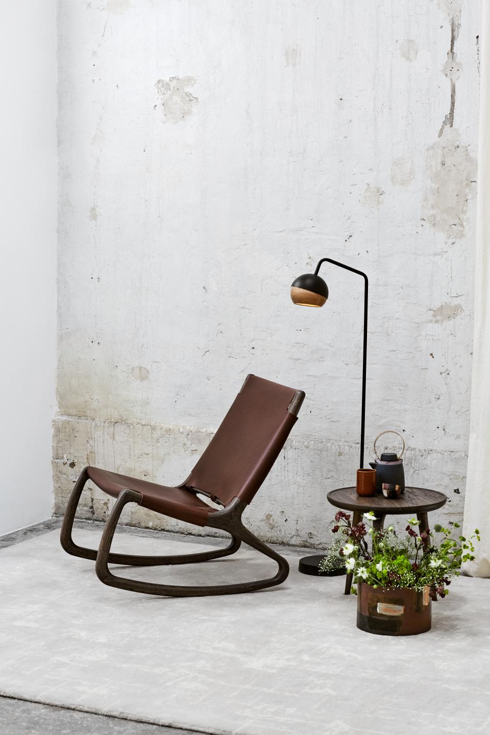 Elegant rocking chair by Mater, designed by Shawn Place, with a sleek modern lamp and decorative plant table.