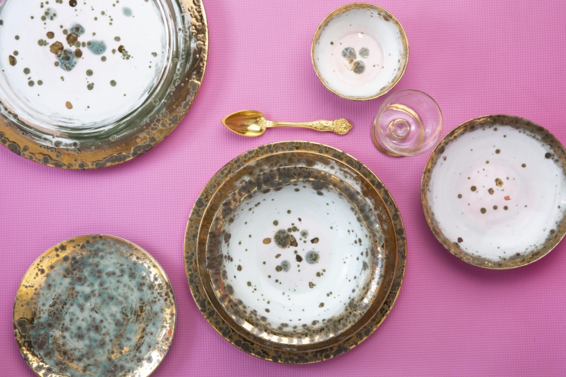 Elegant ceramic dinnerware set featuring intricate gold detailing, displayed on a vibrant pink background for a festive dining experience.