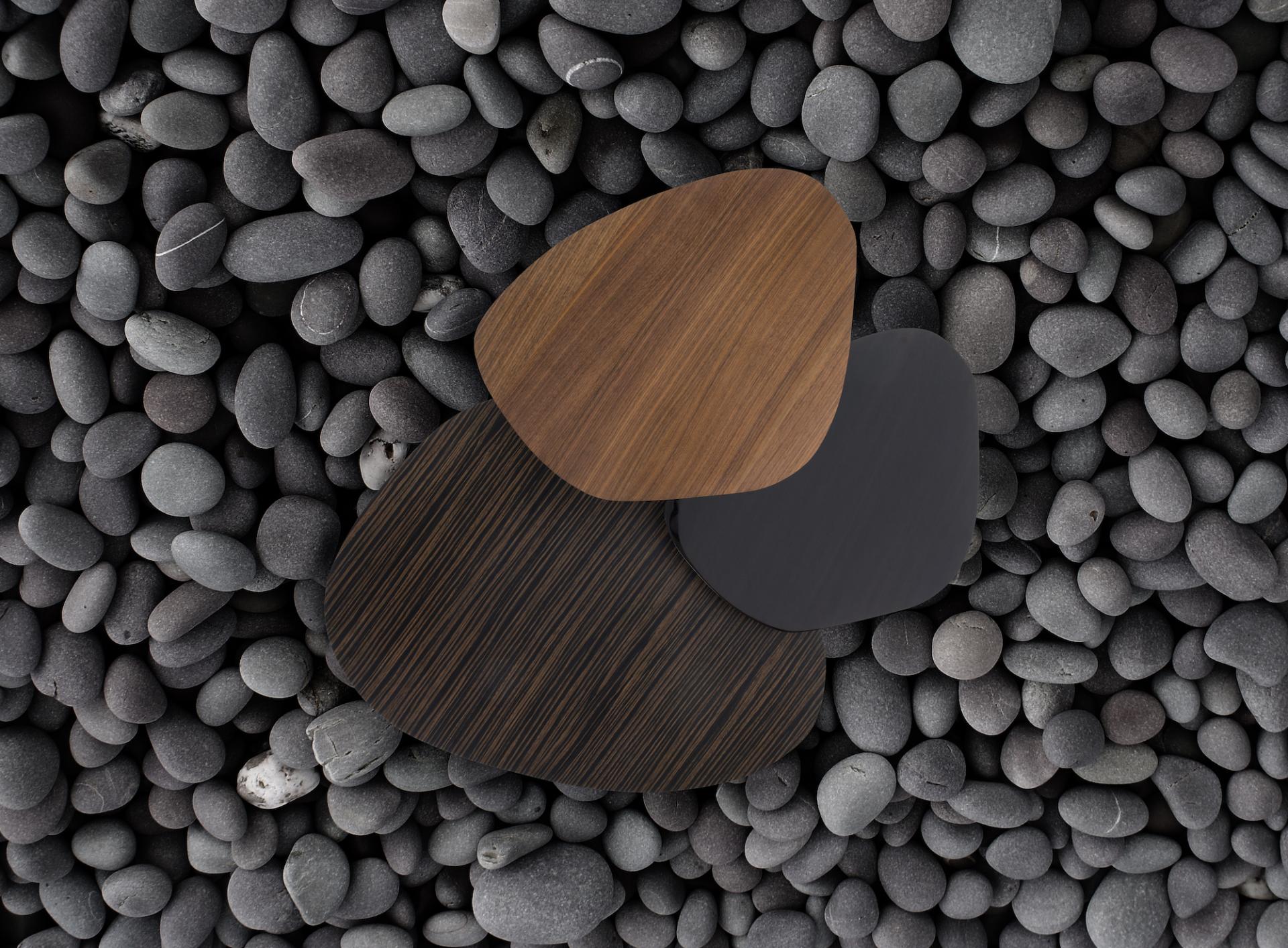 Stylized wooden furniture surfaces in natural tones displayed on a bed of smooth black pebbles, inspired by nature.