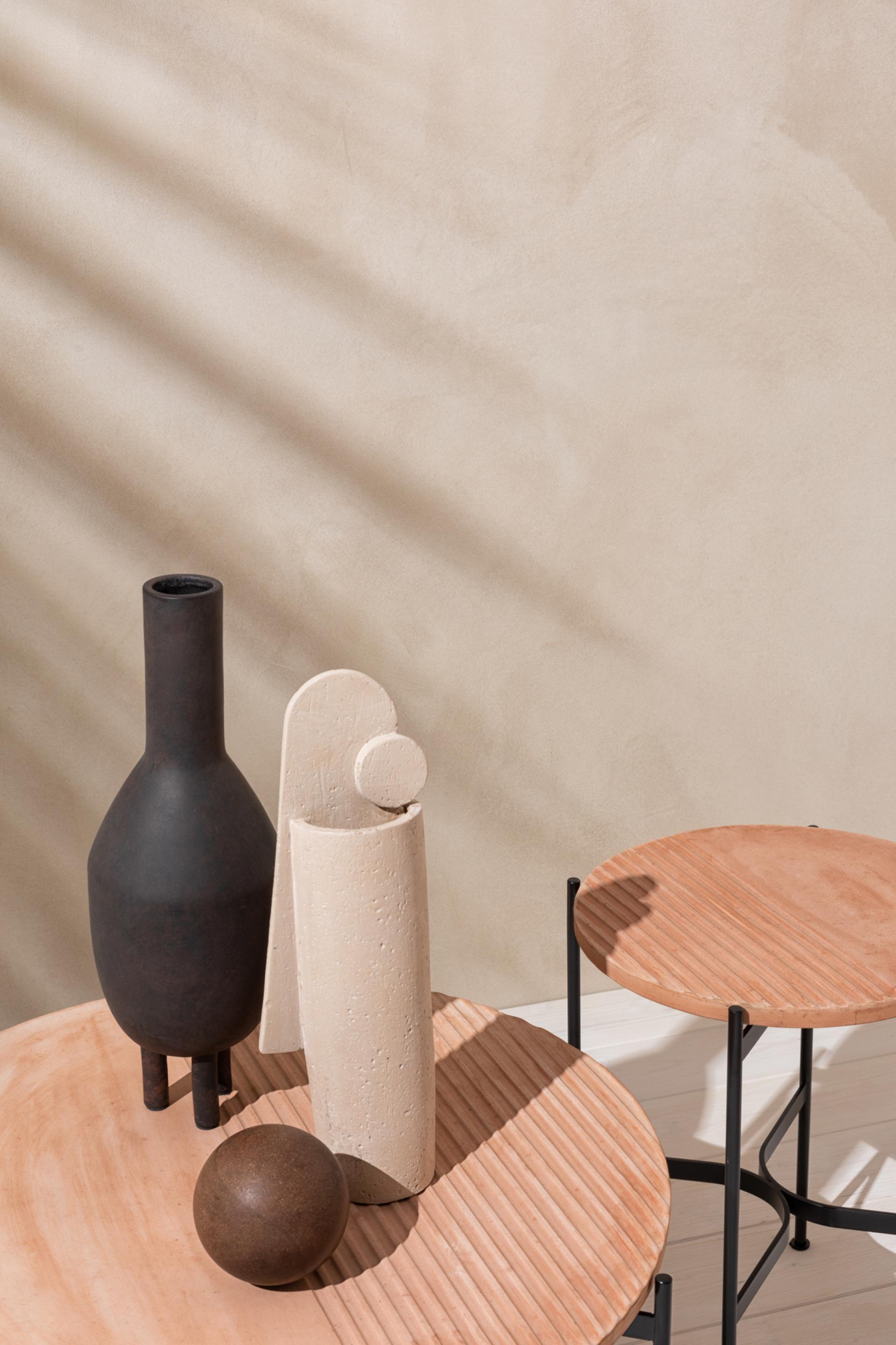 Contemporary ceramic vases and a wooden sphere on a textured round table, showcasing SP01's artistic furniture design.