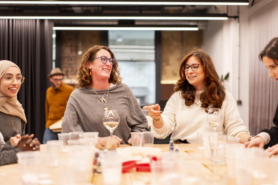 Celebrating creativity at Material Source Studio, women engage in conversation with drinks during a community gathering in Manchester.
