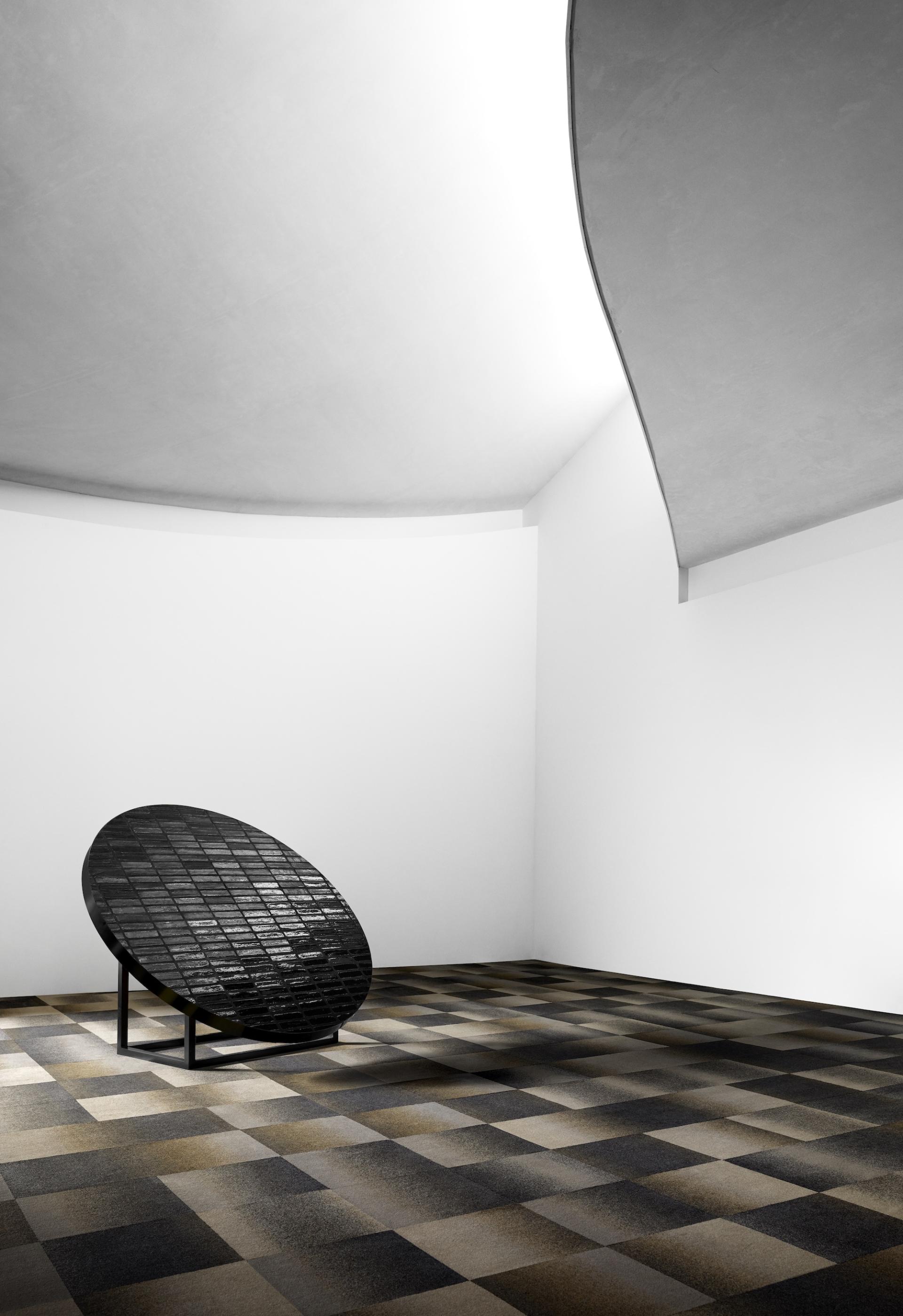 Black circular sculpture on grid-patterned carpet in minimalistic interior, showcasing EGE Carpets x Tom Dixon's Industrial Landscape collection.