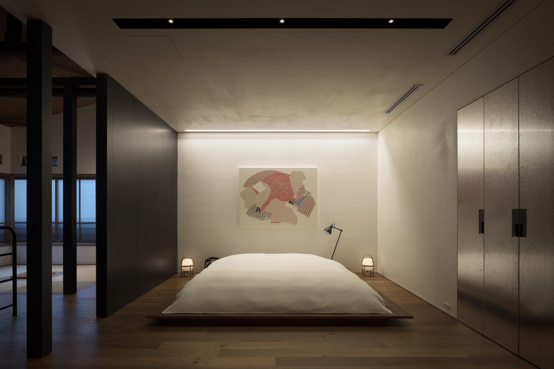 Modern bedroom in TRUNK(HOUSE) featuring minimalist design, wooden flooring, artwork, and ambient lighting in Tokyo.