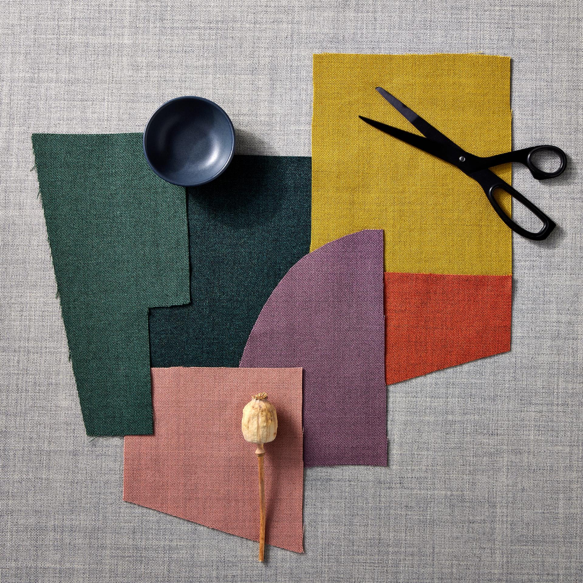Wool fabric swatches in various colors, scissors, a bowl, and a decorative stem on a textured background.