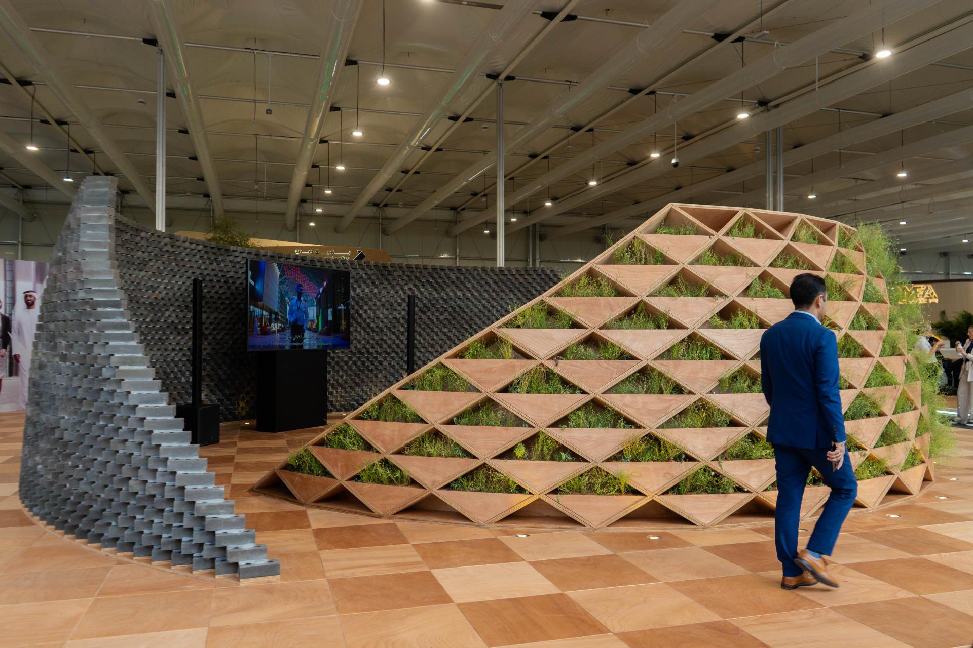 A modern exhibition space showcasing K-BRIQ's sustainable brick design, featuring green plant growth and innovative building materials.