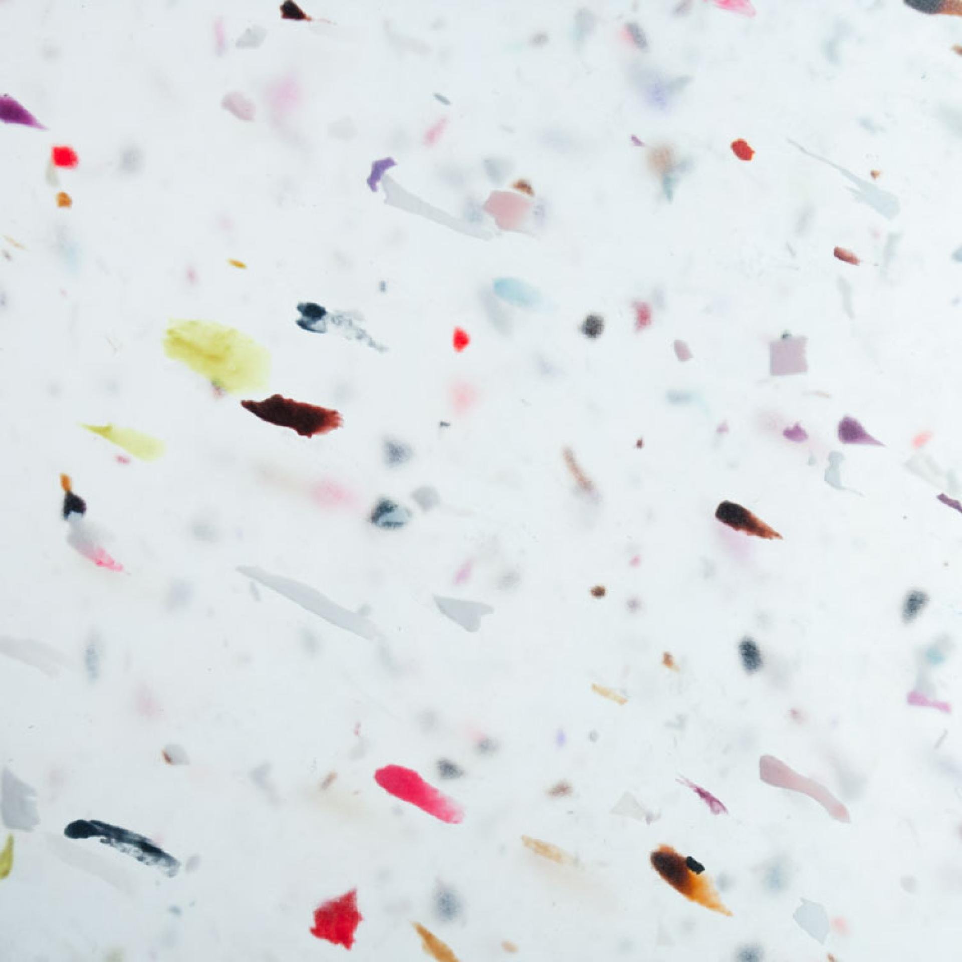 Colorful recycled plastic flakes suspended in a clear background, showcasing innovative materials by Smile Plastics for SDS 2022.