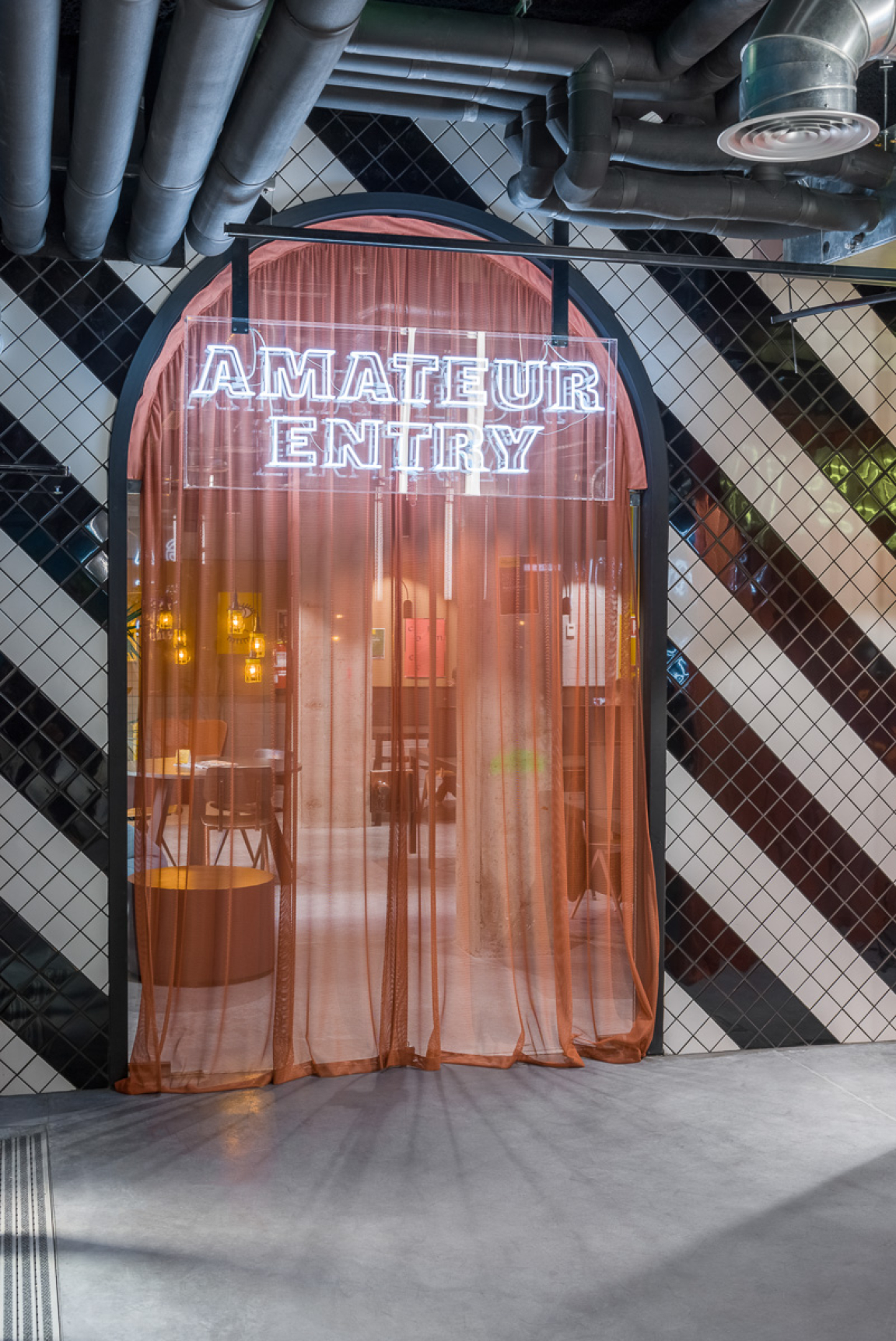 Neon sign reading "Amateur Entry" framed by sheer curtains in Masquespacio-designed co-living space in Barcelona.