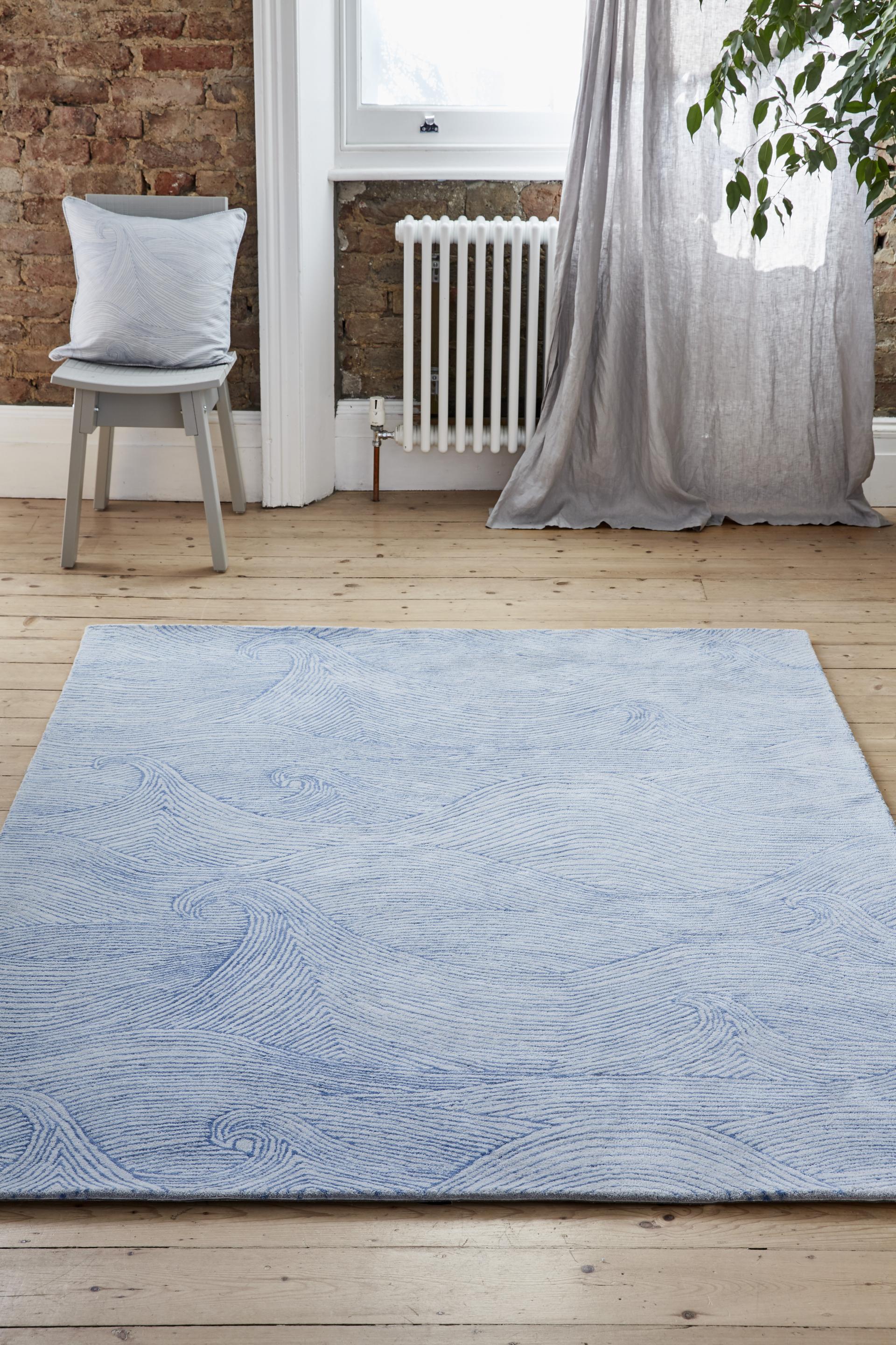 Stylish blue patterned rug on wooden floor beside a chair and window, reflecting nature-inspired design aesthetics.
