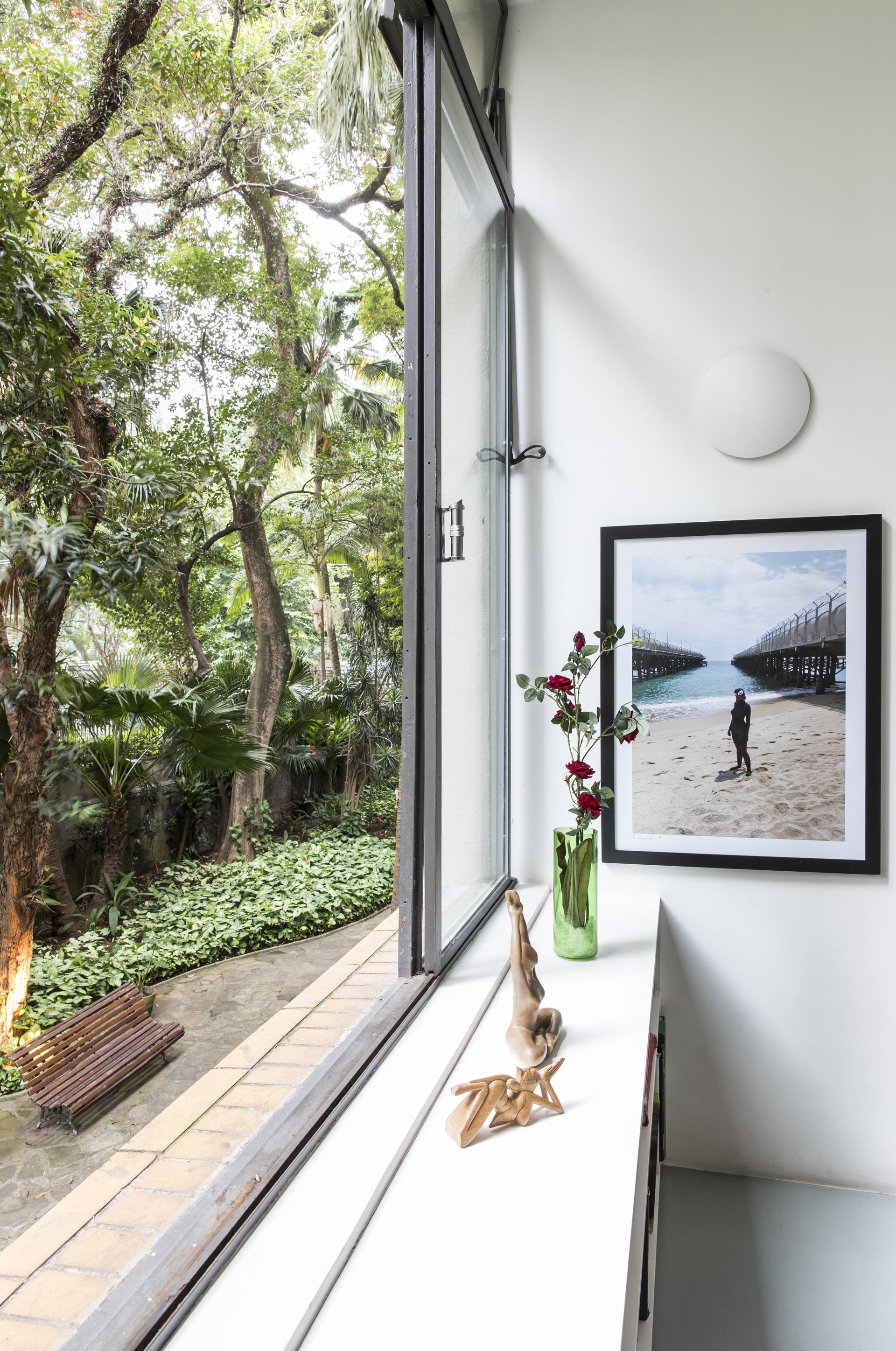 Sunlit interior of a renovated 1950s São Paulo apartment, featuring a scenic garden view and artistic decor.