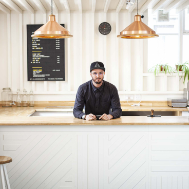Barista at a modern coffee shop, featuring a sleek countertop and menu board showcasing specialty coffee offerings.