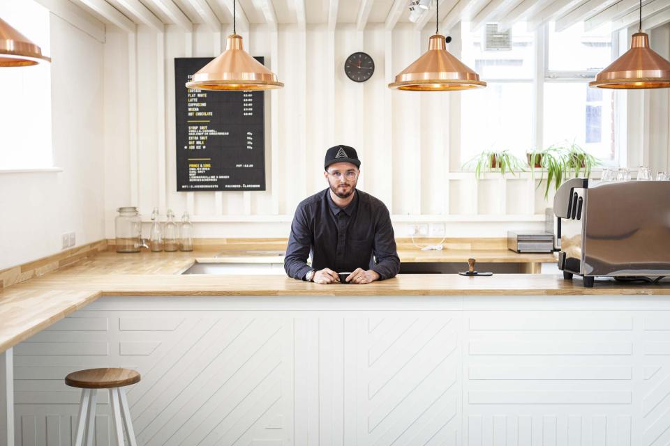 Barista at a modern coffee shop, featuring a sleek countertop and menu board showcasing specialty coffee offerings.