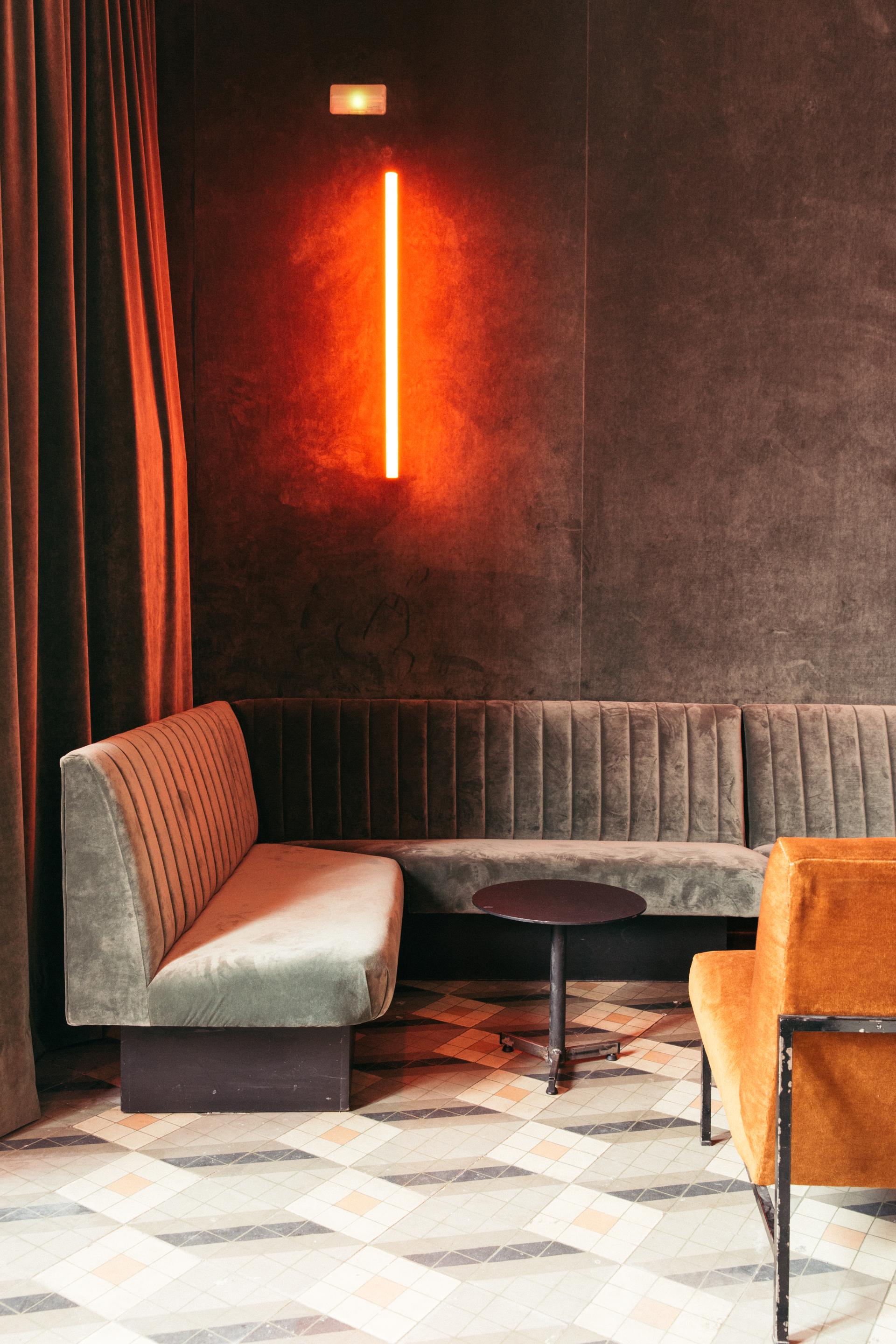 Stylish interior featuring velvet seating, a round table, and a vibrant neon light, inspired by retro Americana design.