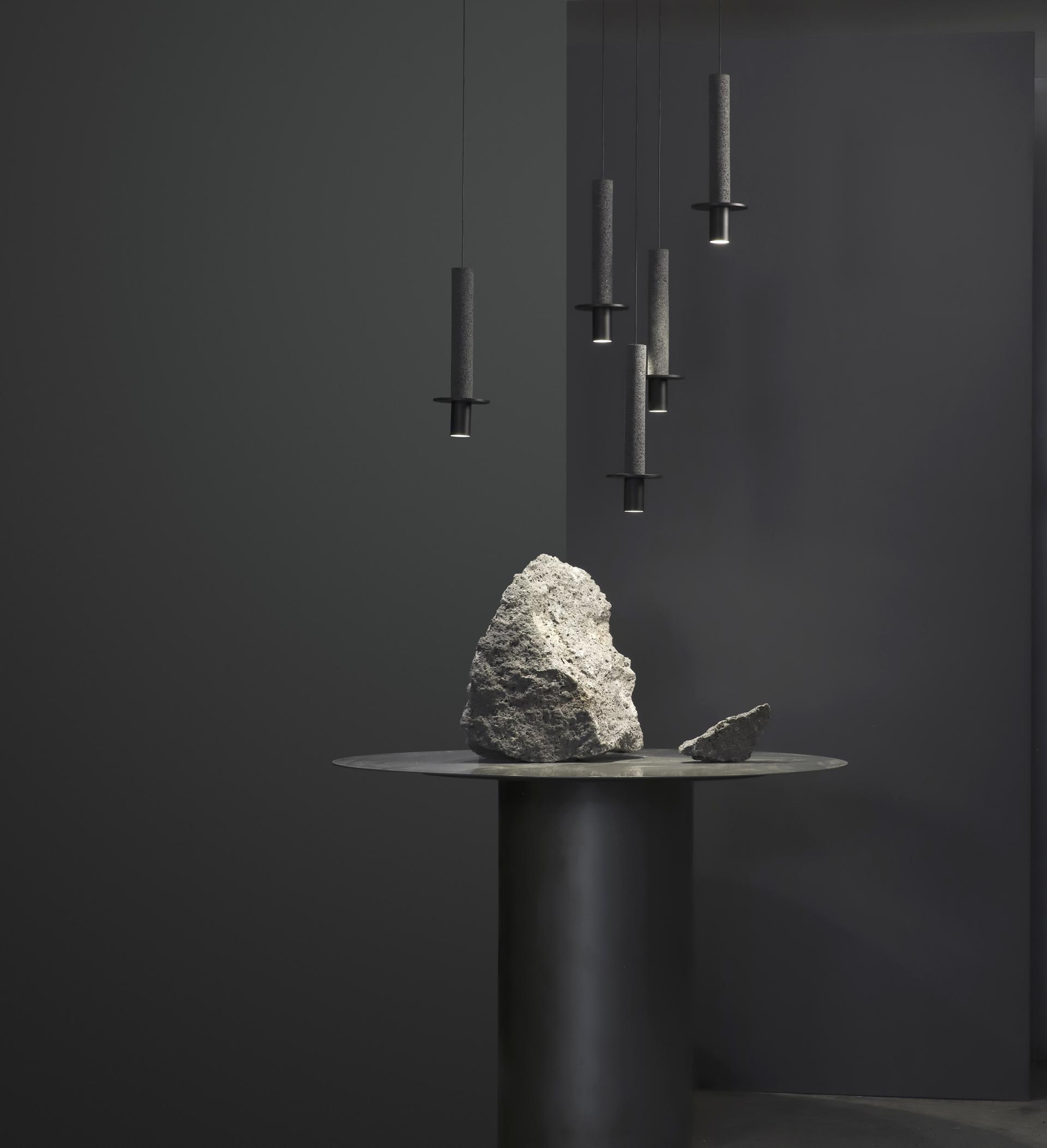 Modern lighting fixtures hang above a minimalist table with sculptural rocks, showcasing studio davidpompa's Meta collection.