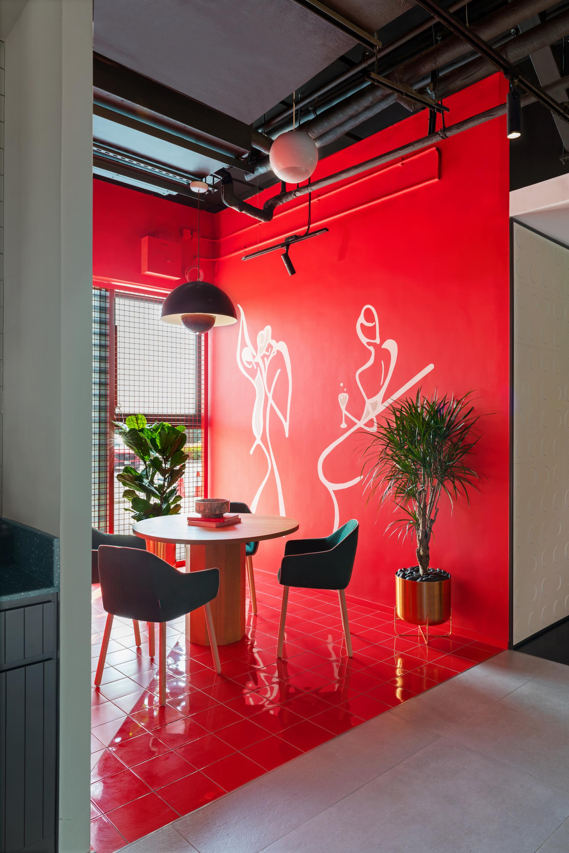 Vibrant dining area featuring a round wooden table, playful wall art, and modern green chairs against a striking red backdrop.