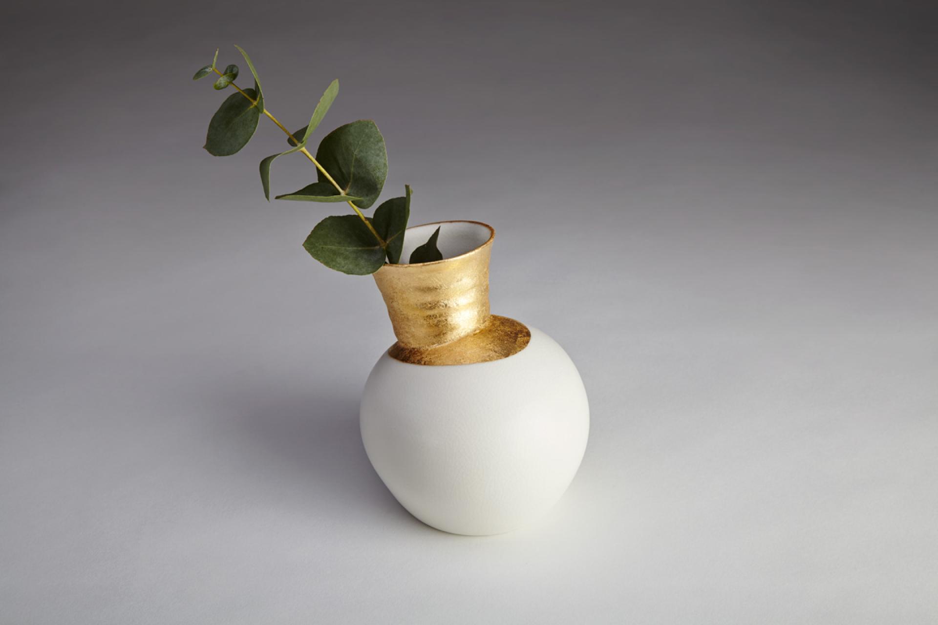 Elegant ceramic vase with a gold accent, featuring lush green eucalyptus leaves, showcased at the London Art Fair 2019.