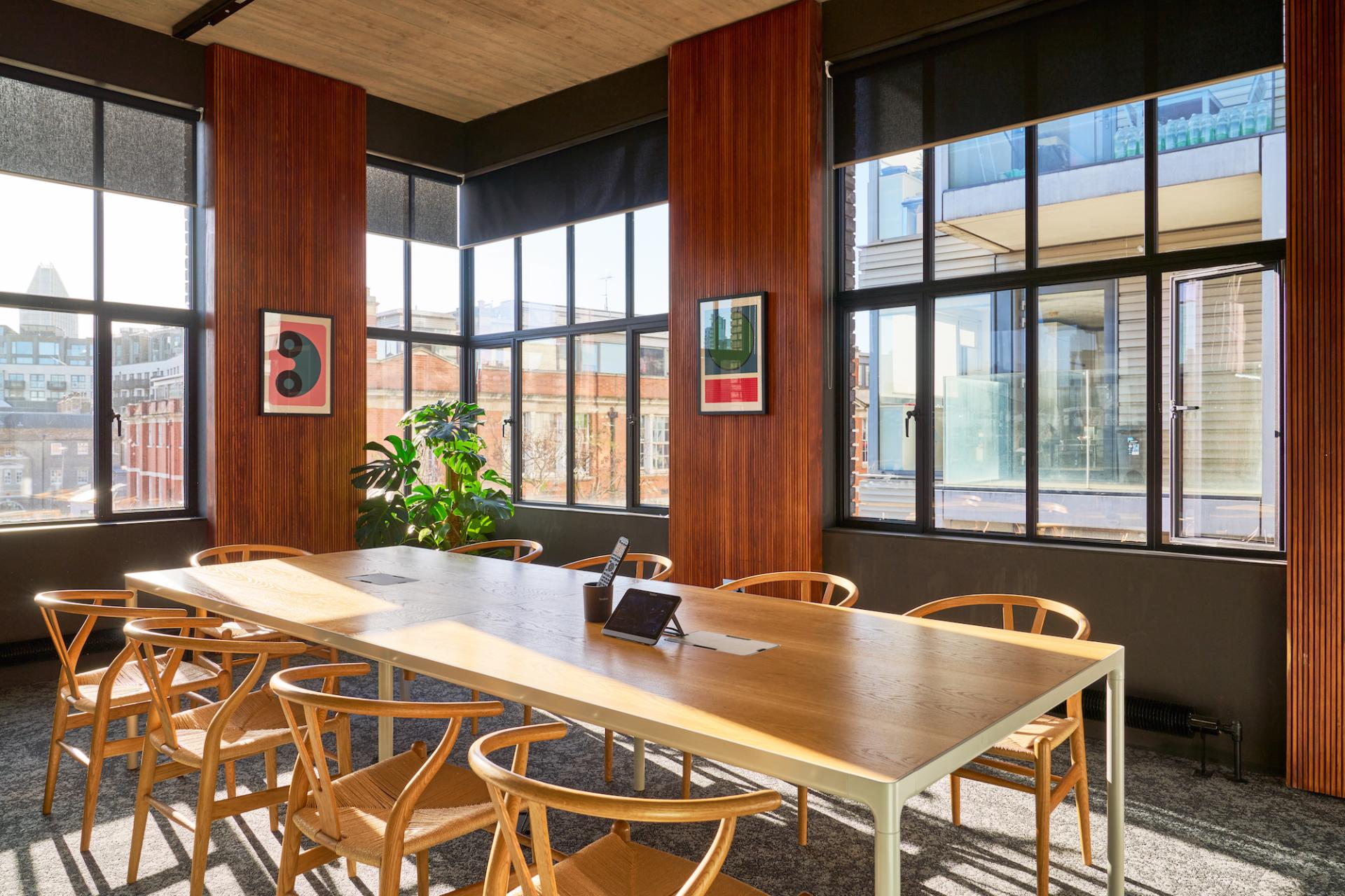 Modern workspace with large windows, wooden accents, a long table, and greenery, representing sustainable office design for Joseph Joseph.