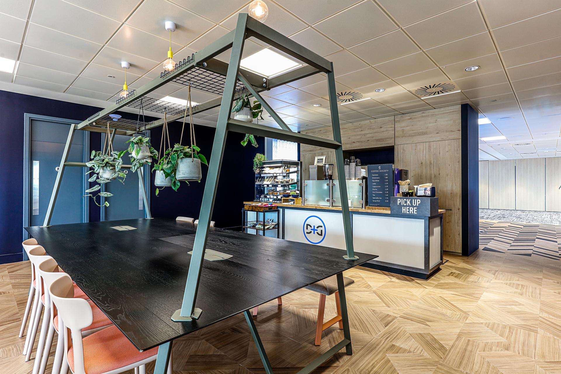 Modern office space at Domestic & General featuring a communal table with plants and a coffee area, showcasing innovative design.